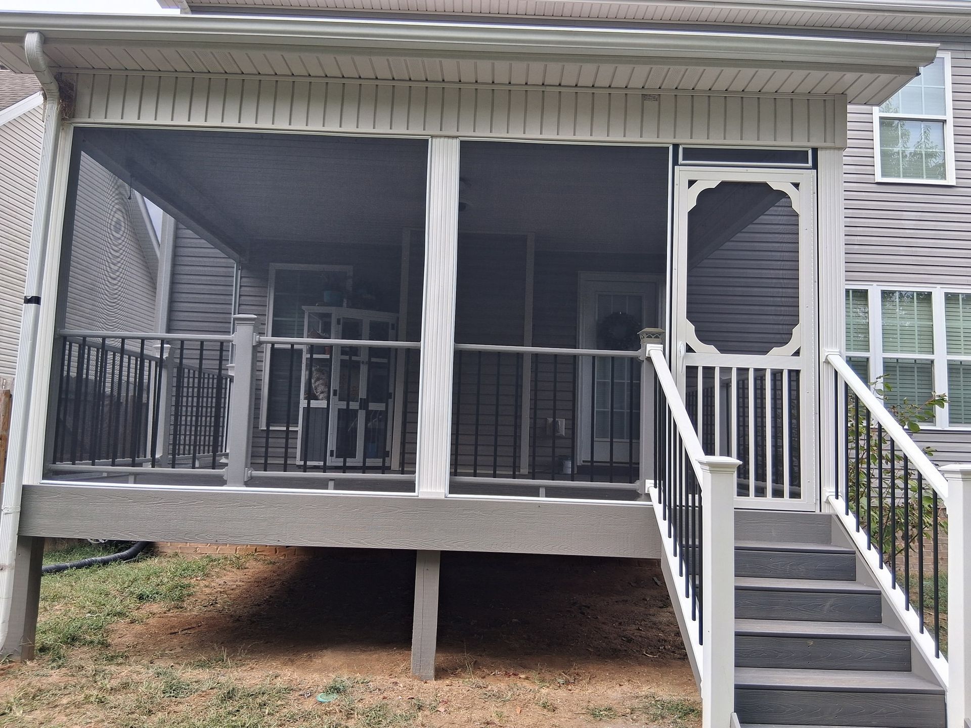 Screened-in porch with steps, black railing, and gray siding.  White trim. Brown yard.