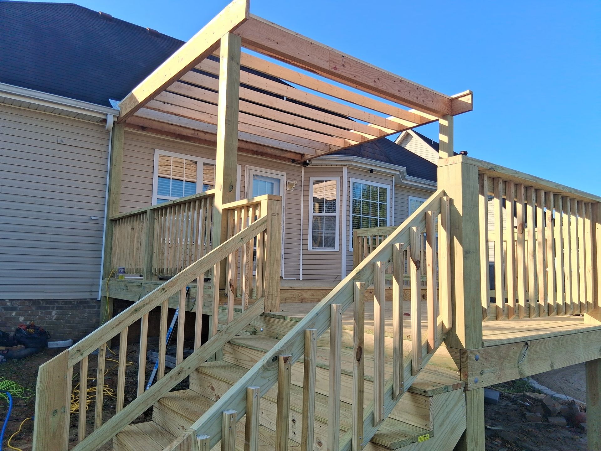 Wooden deck with stairs, a pergola, and siding on the back of a house.