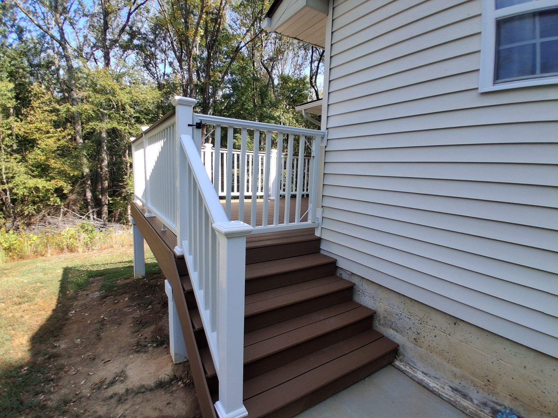 Wooden deck with white railing and steps leading to a house with white siding.
