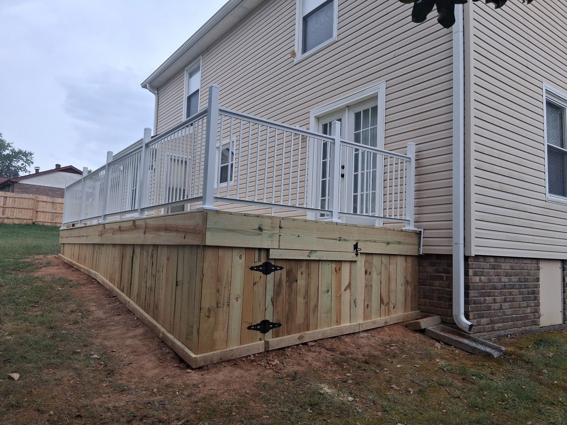 Wooden deck with white railing attached to a beige house, next to grass.
