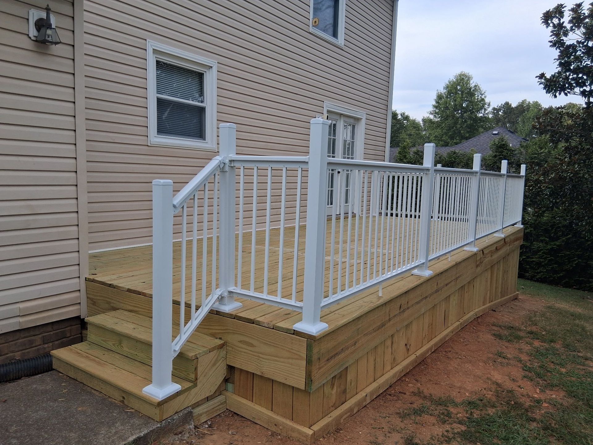 New wooden deck with white railing attached to a beige house, steps leading to the deck.