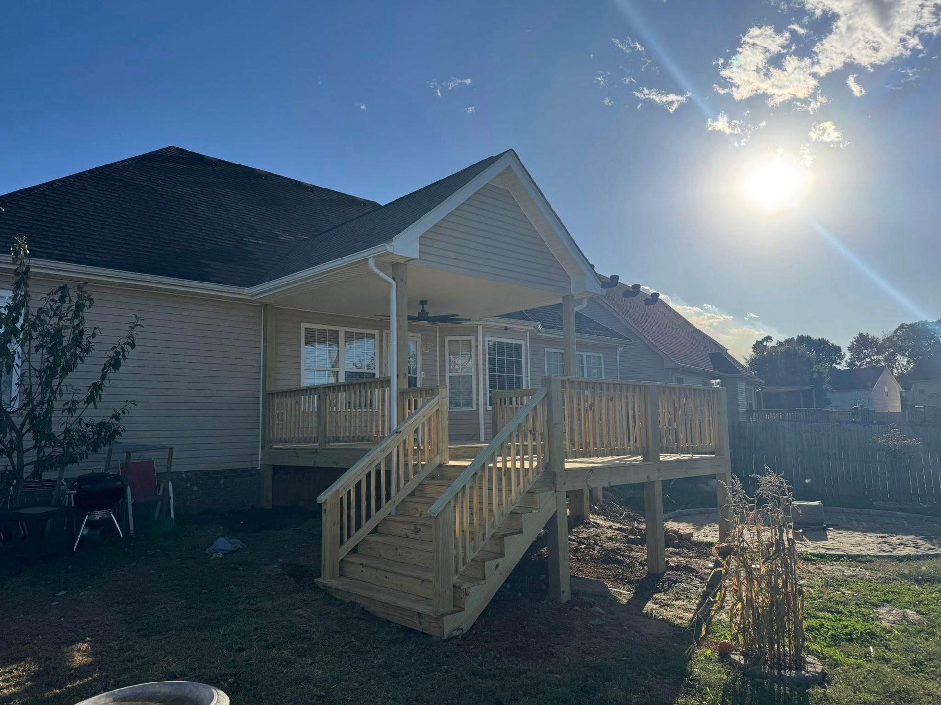 A wooden deck with stairs attached to a tan house under a bright sky.