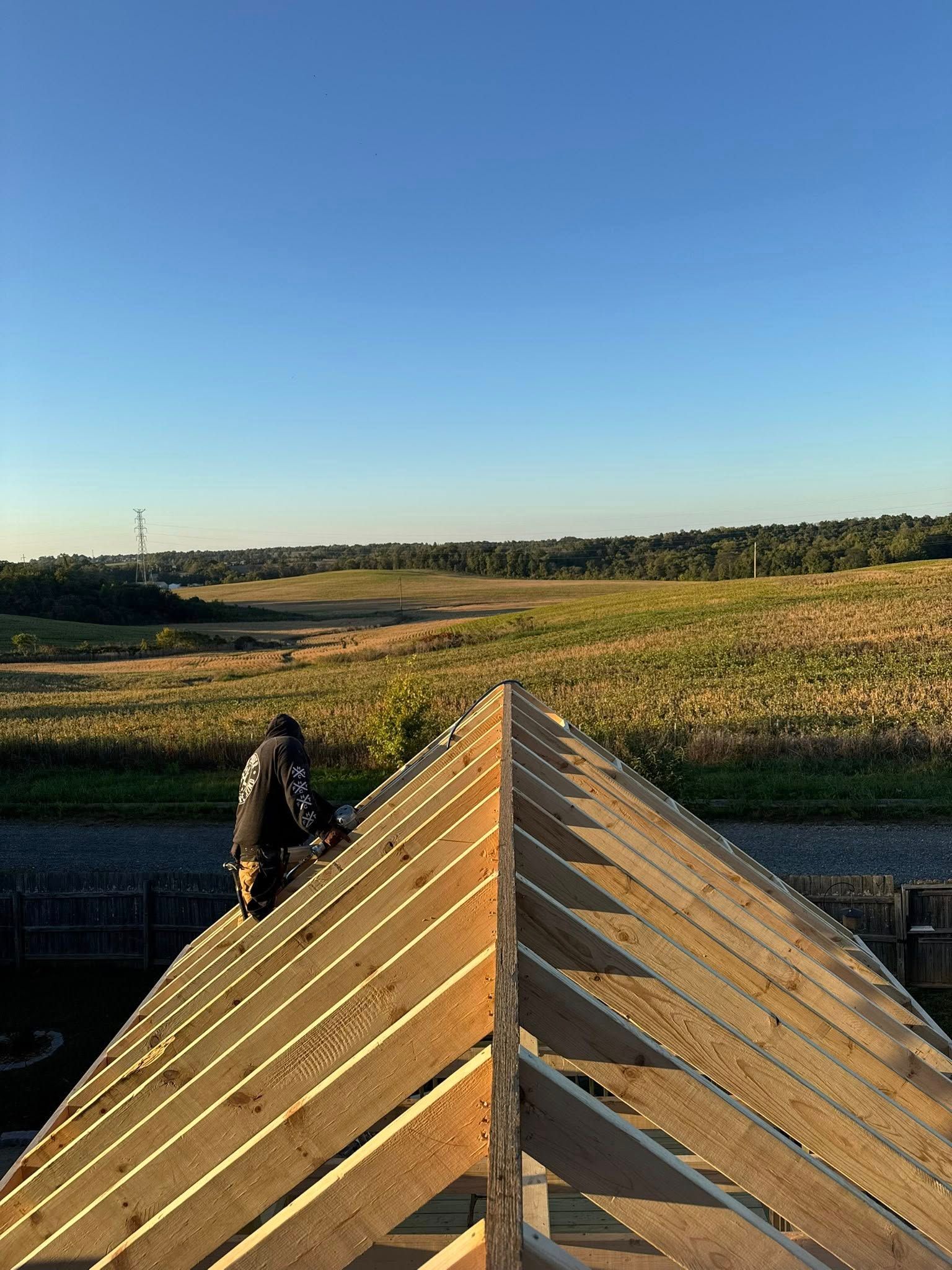 Carpenter working on roof, sunny day, field in background.