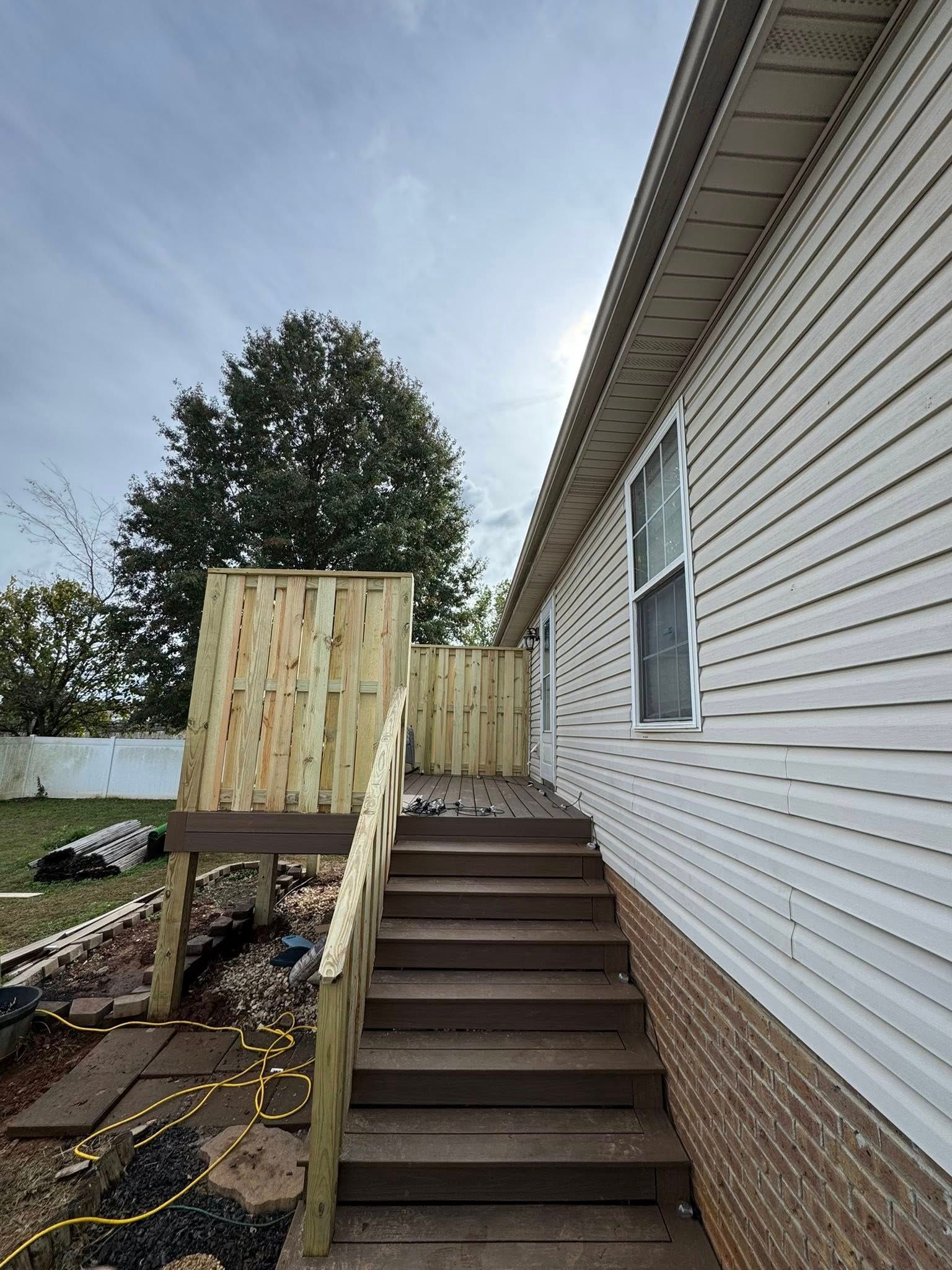 Wooden deck with stairs, fence, and access to a house. Cloudy sky overhead.