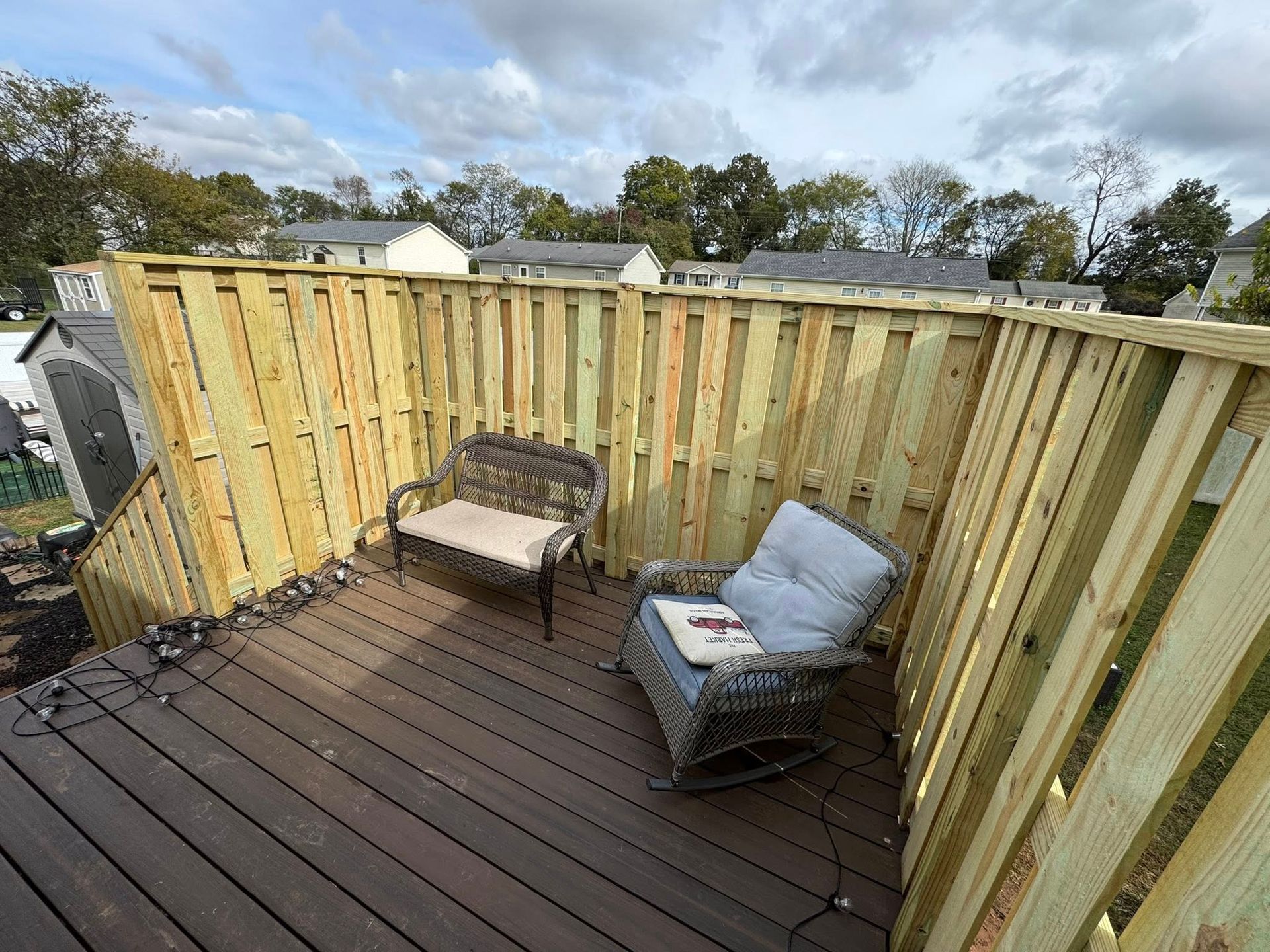 Wooden deck with seating against a wooden fence, under a cloudy sky.