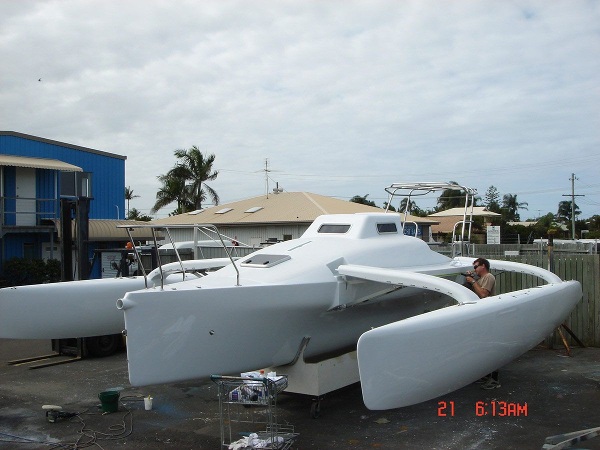 A Man Is Standing Next to A White Boat — Ashby Boat Builders In Buddina, QLD