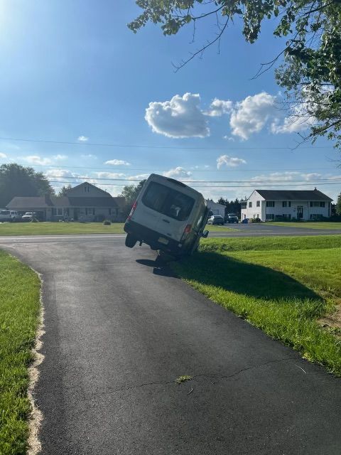 White van tilted on its side off a driveway, grass and blue sky background.