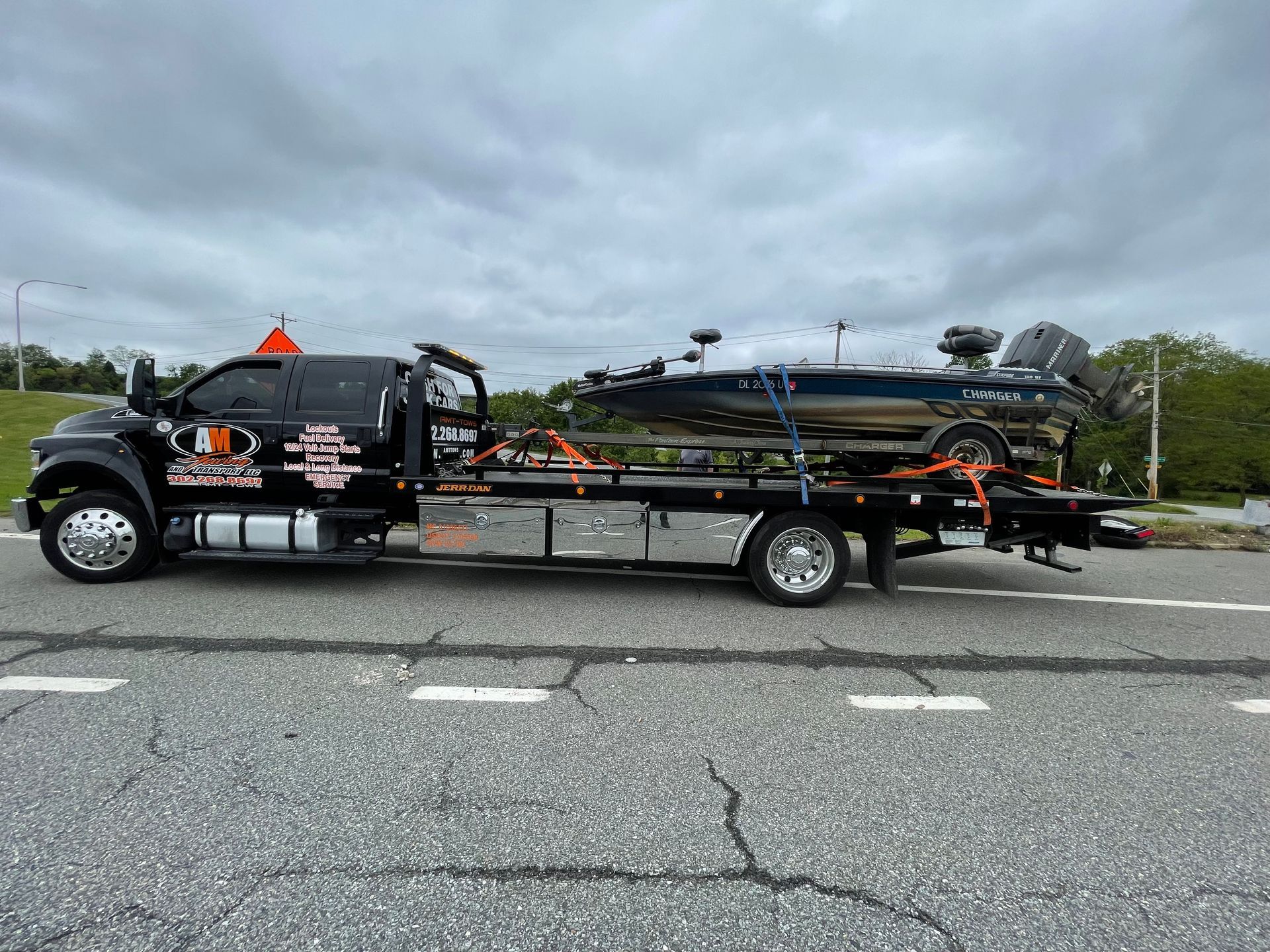 Tow truck carrying a black boat on a flatbed, on a road.