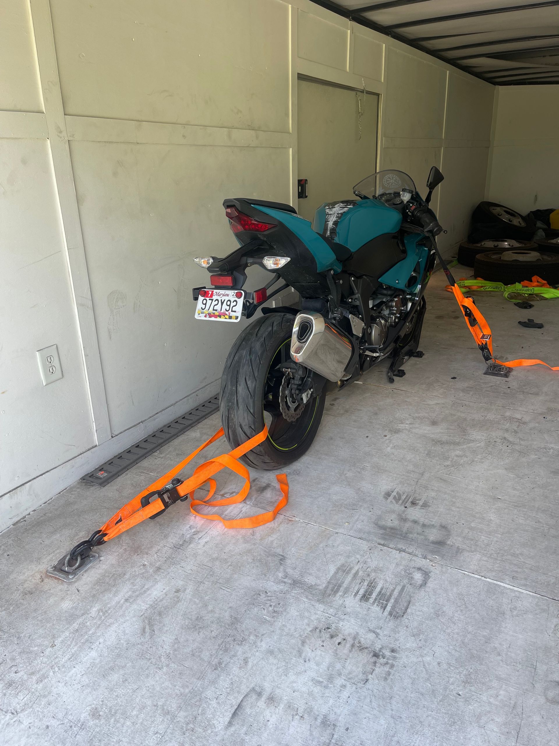 Teal sport motorcycle secured with orange straps inside a trailer.
