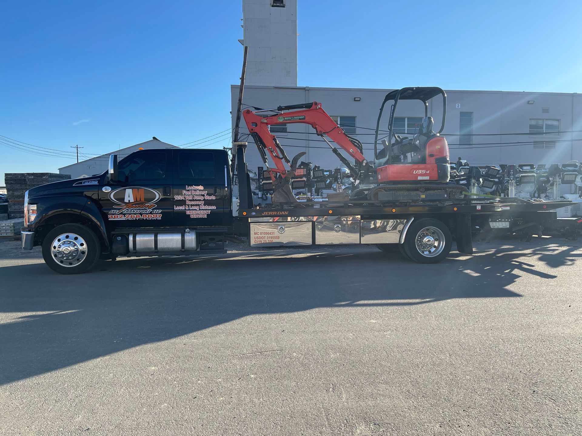 Tow truck operator securing a silver hatchback onto a flatbed, wearing safety vest.