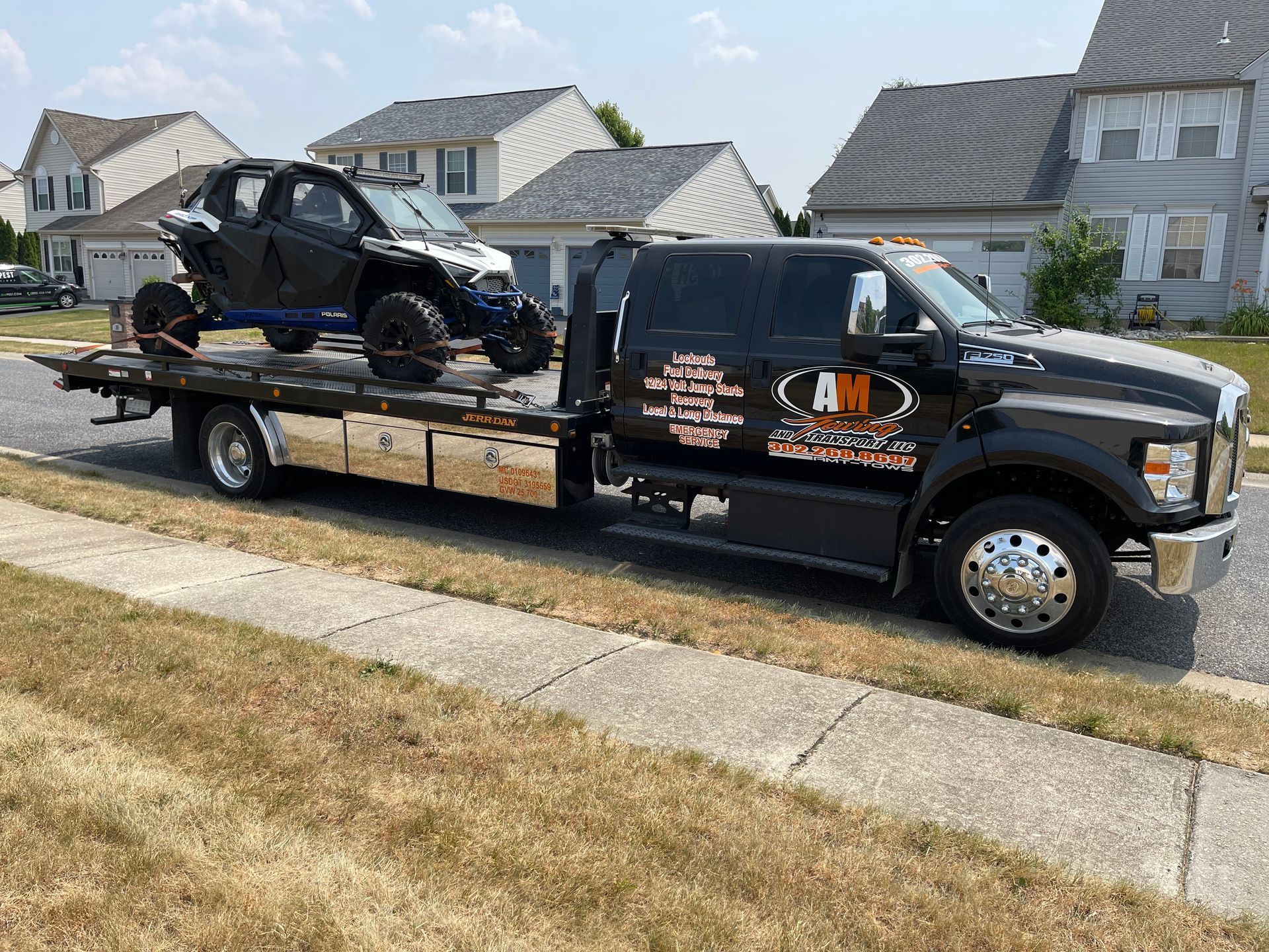 Black tow truck hauling a side-by-side vehicle on a sunny residential street.
