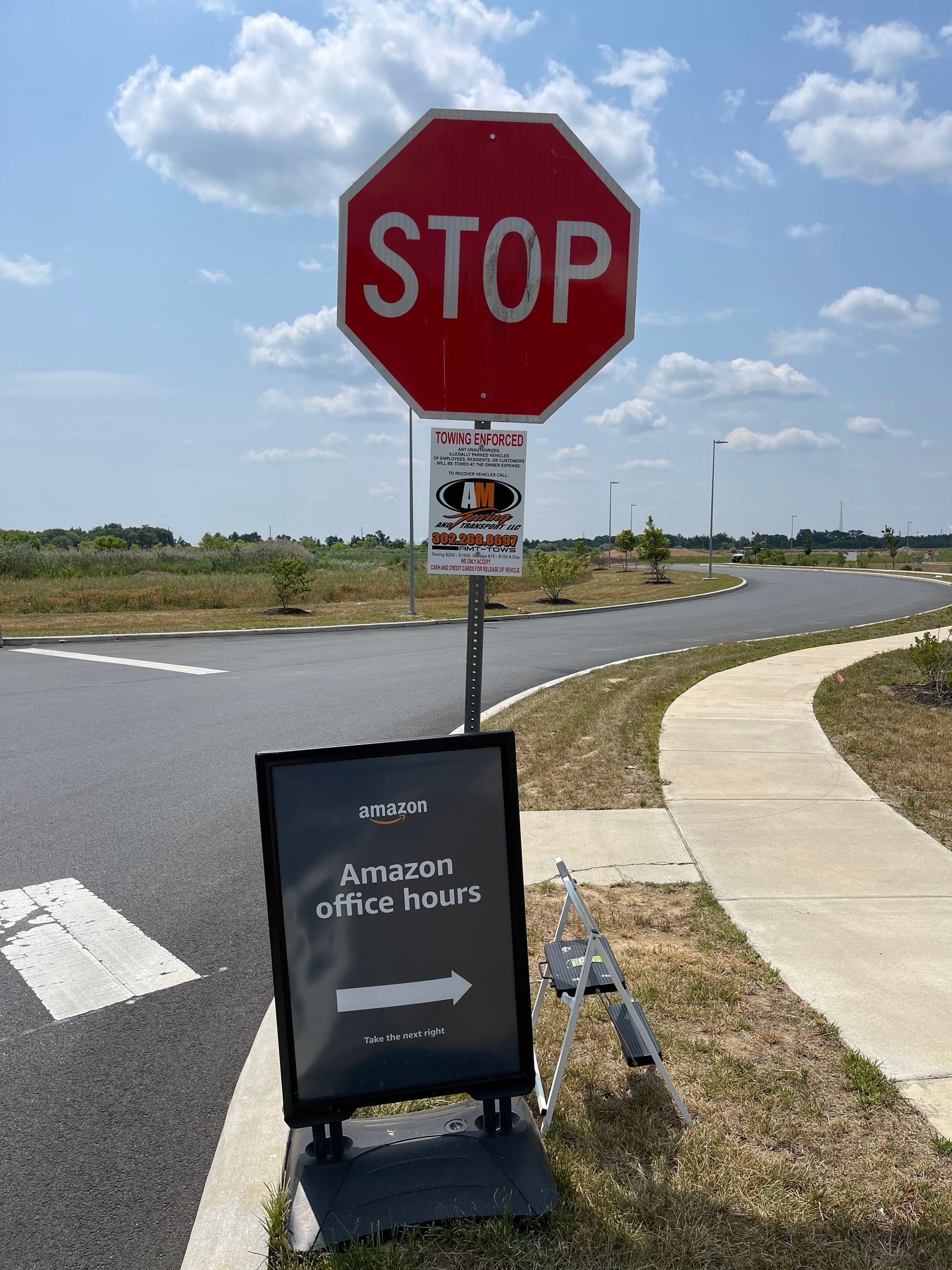 Stop sign, with a sign indicating Amazon office hours. Paved road and sidewalk.