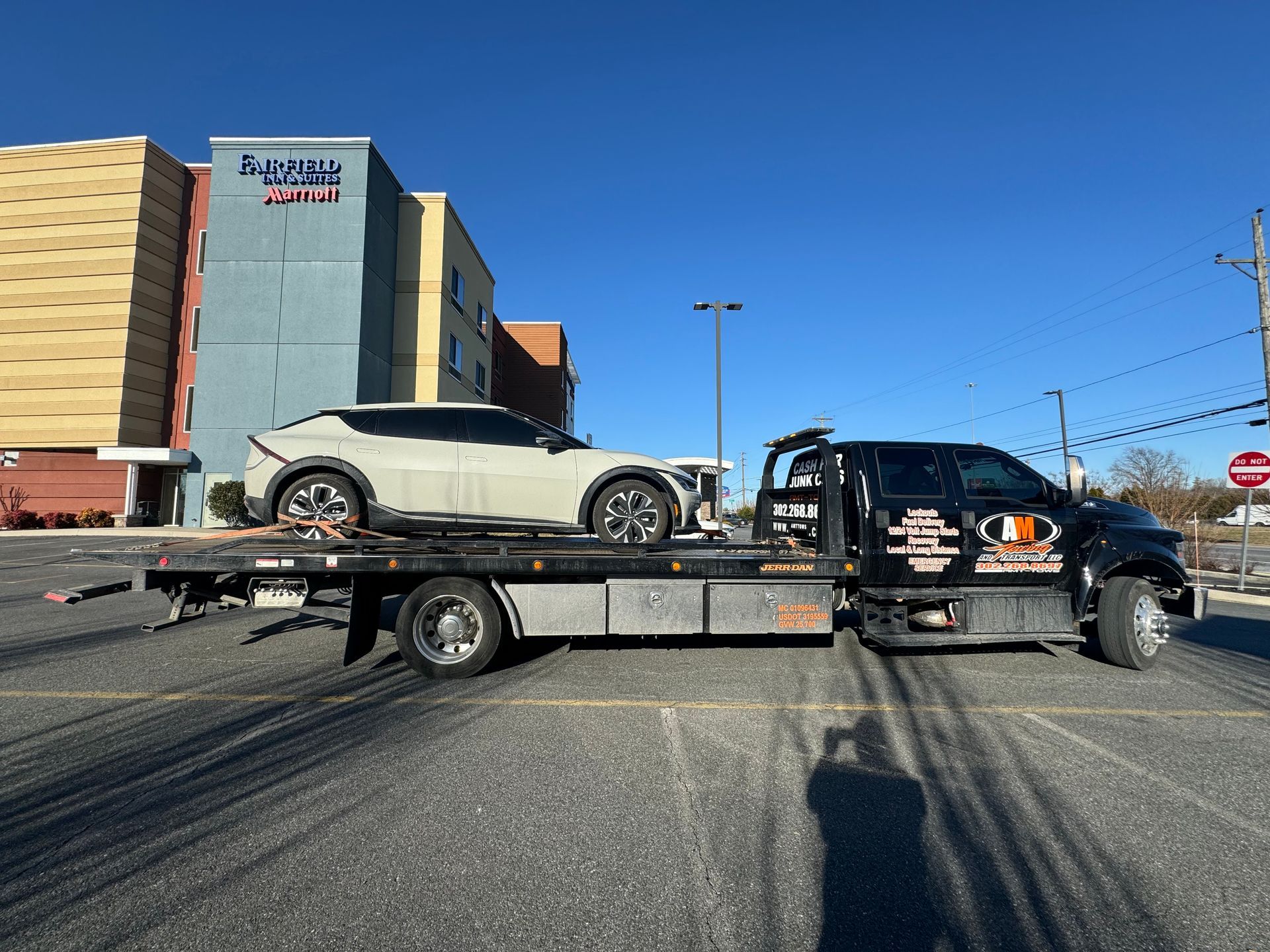 Tow truck with a white car on its flatbed in a parking lot. Hotel in the background.