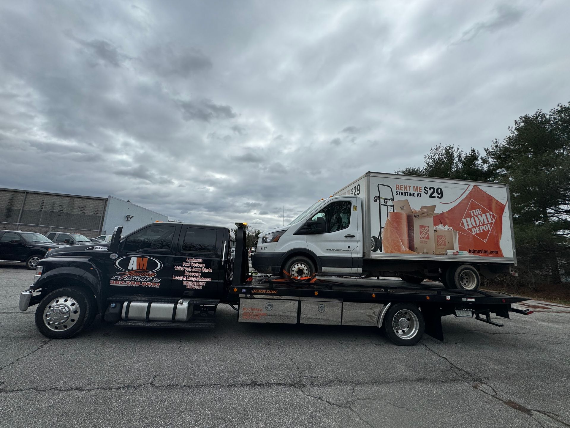 Tow truck carrying a white cargo van on a cloudy day.