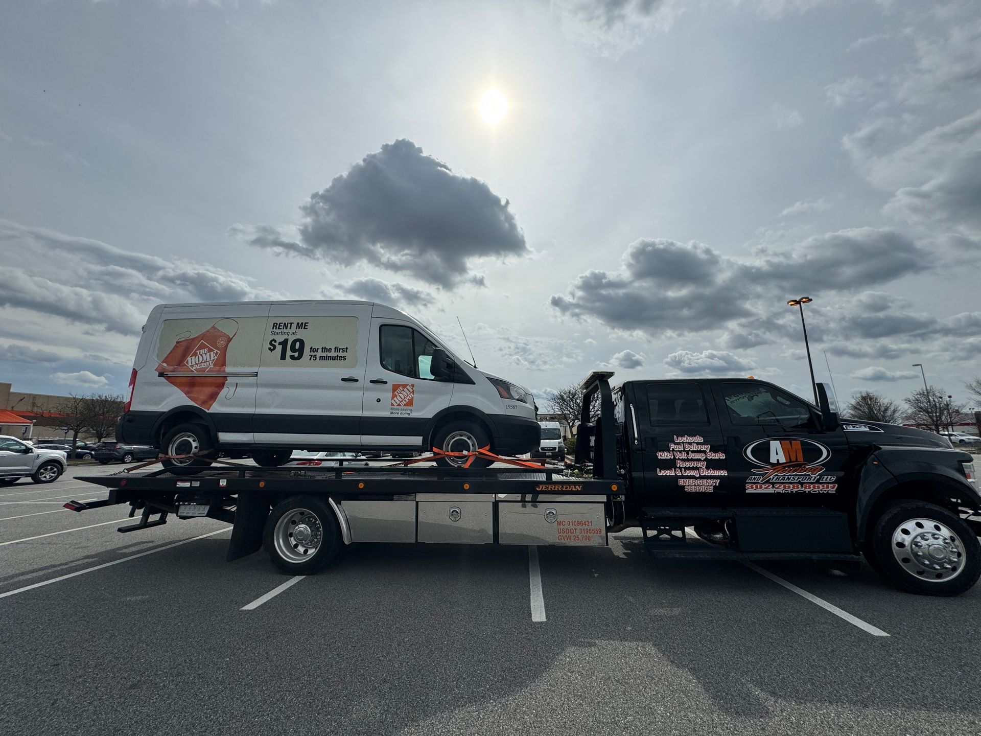Tow truck carrying a white Home Depot van on a sunny day in a parking lot.