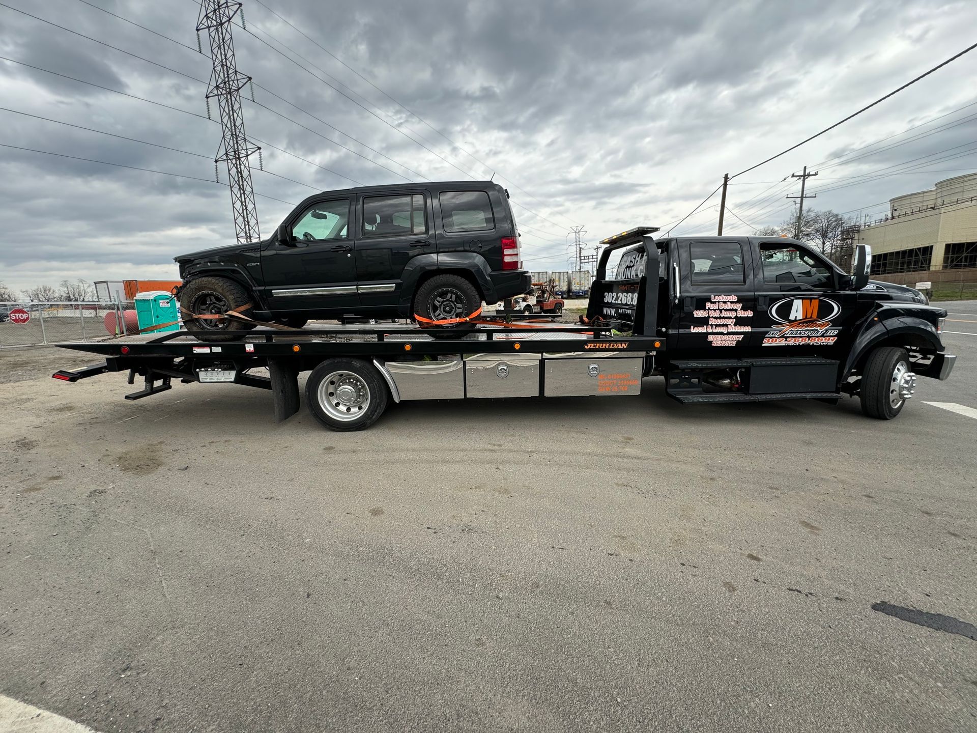 Black SUV on a black tow truck in an outdoor setting with a cloudy sky.