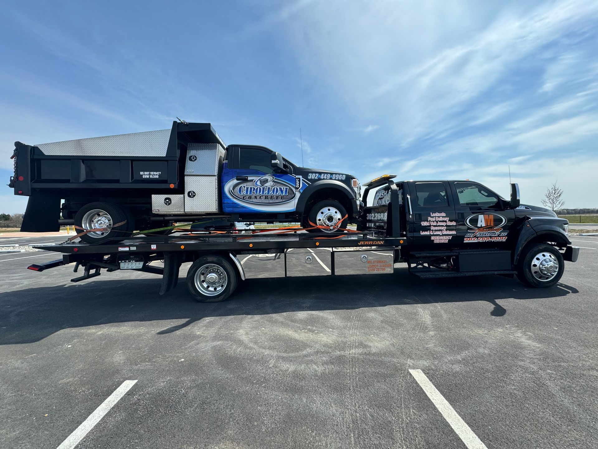 Tow truck hauling a dump truck on a sunny day. Both vehicles are black, with company logos.