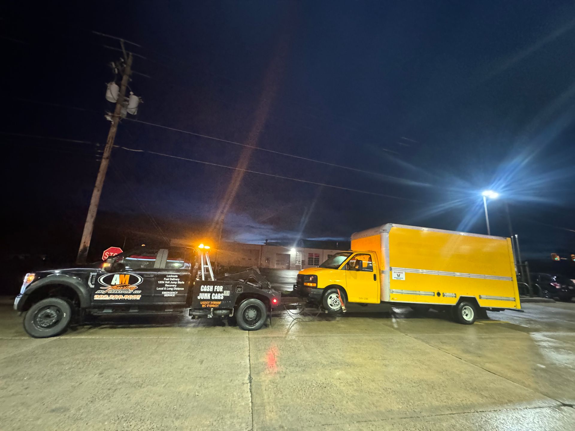 Tow truck towing a yellow box truck at night.