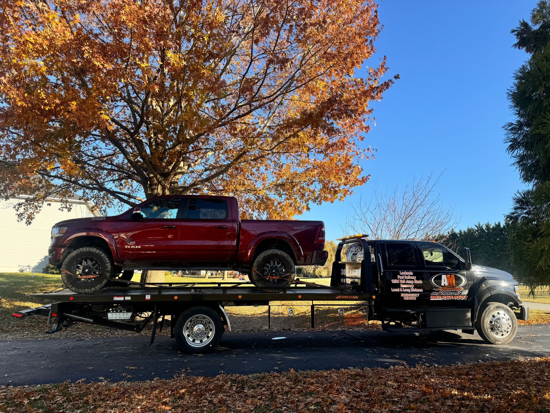 Red pickup truck being transported on a black flatbed tow truck on a road with fall foliage.