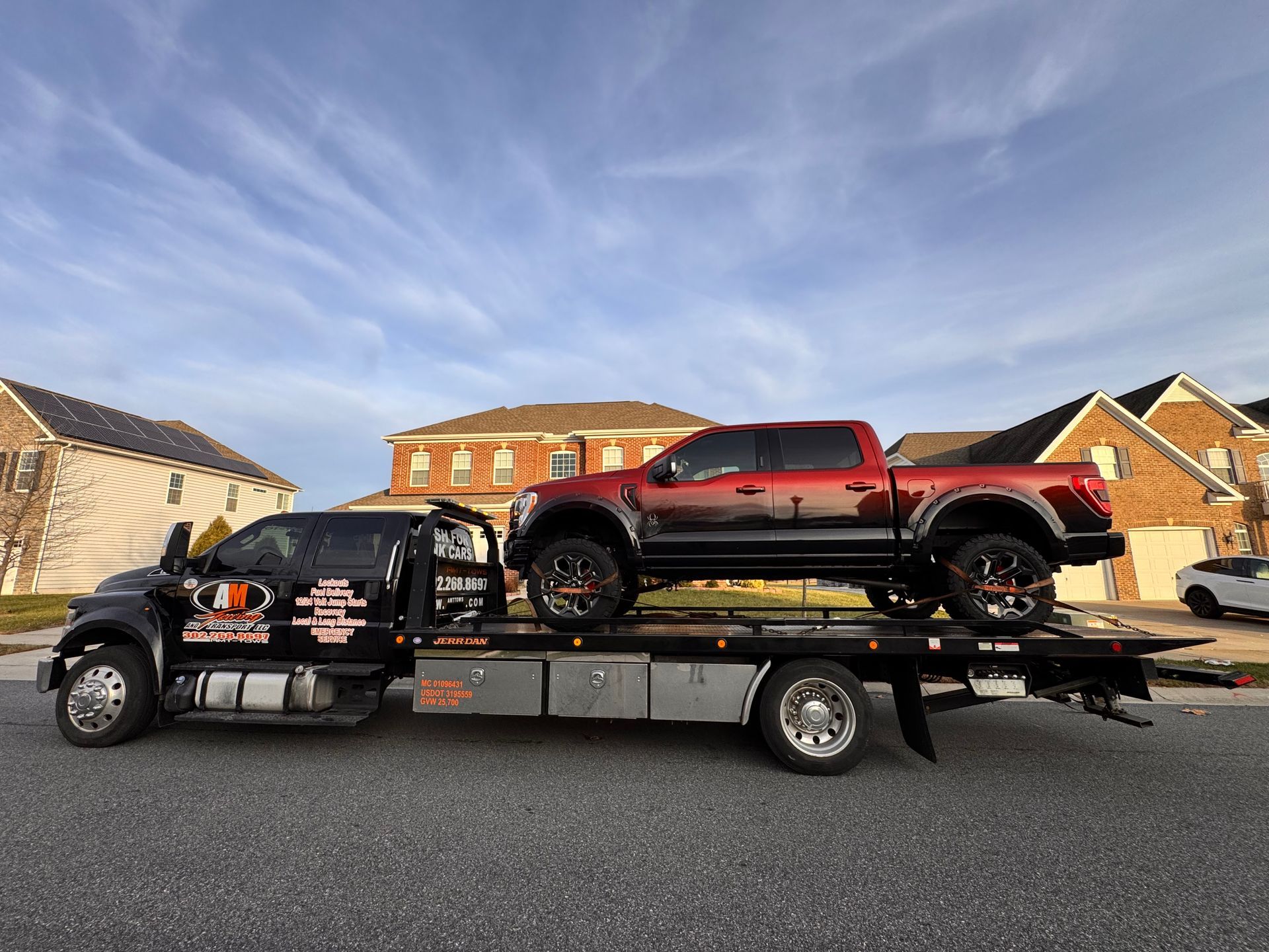 Tow truck hauling a red pickup truck on a residential street; bright day.