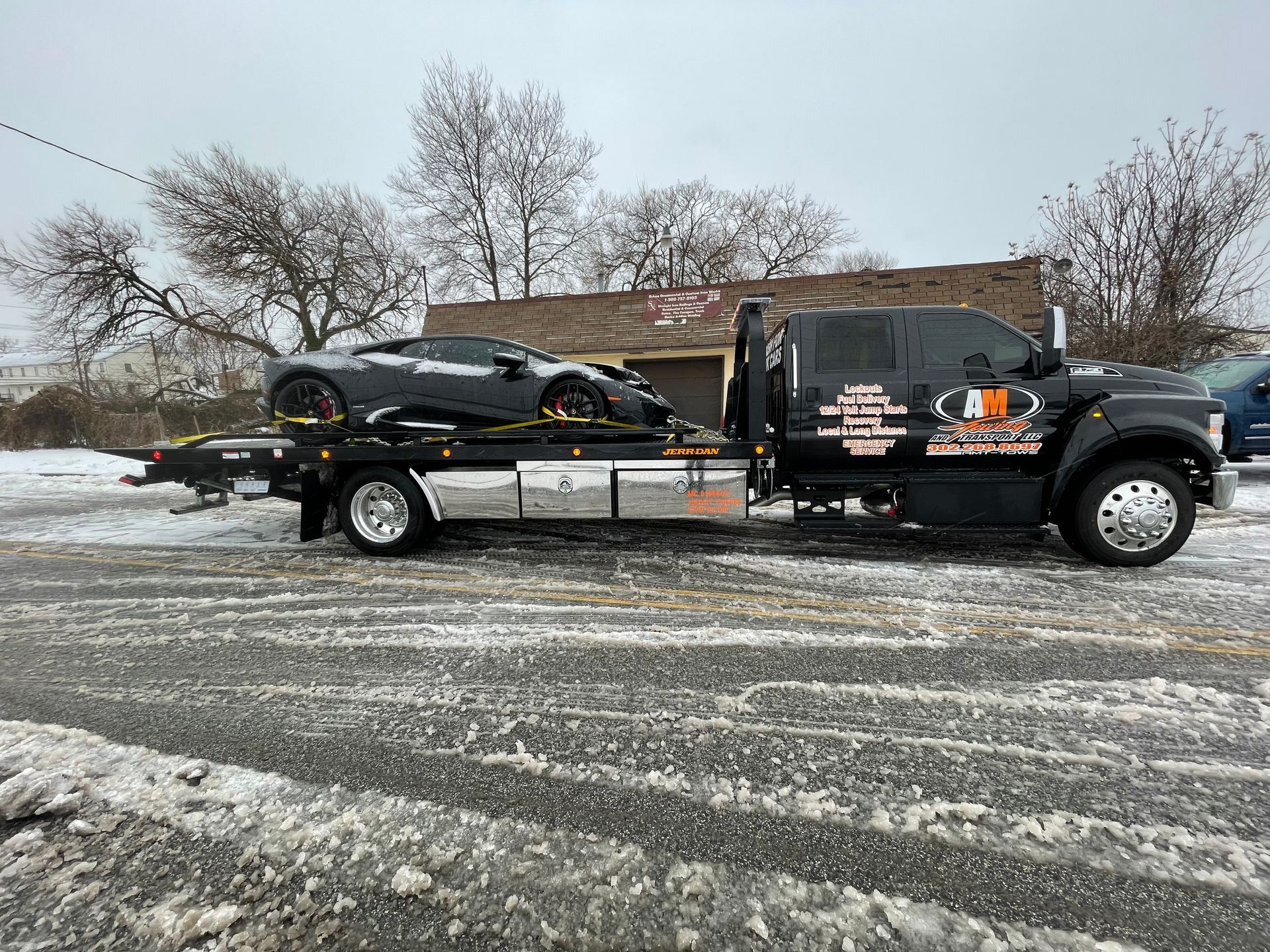 Black sports car on a black tow truck in a snowy environment.