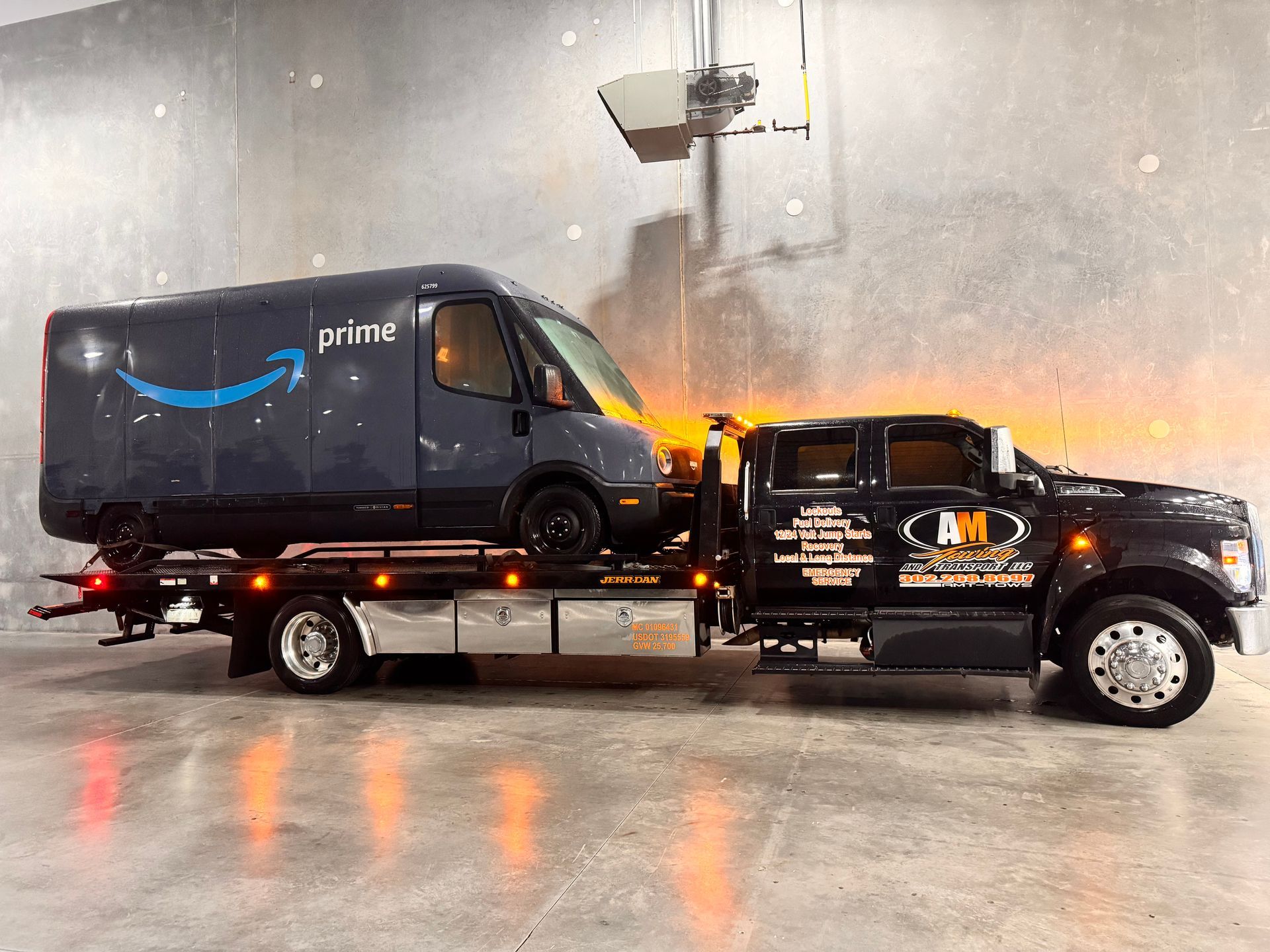 Amazon delivery van loaded onto a black tow truck inside a building.