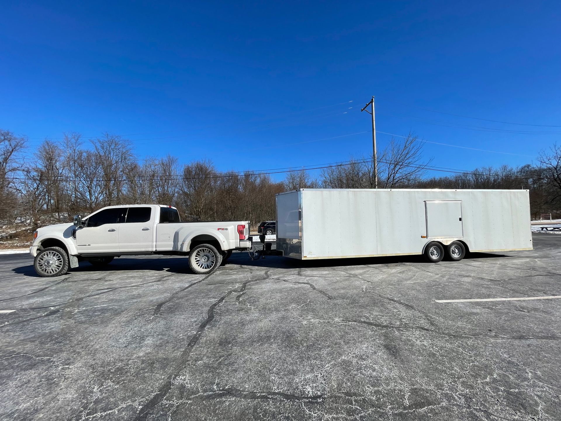 White truck towing a white enclosed trailer in a snowy parking lot under a blue sky.