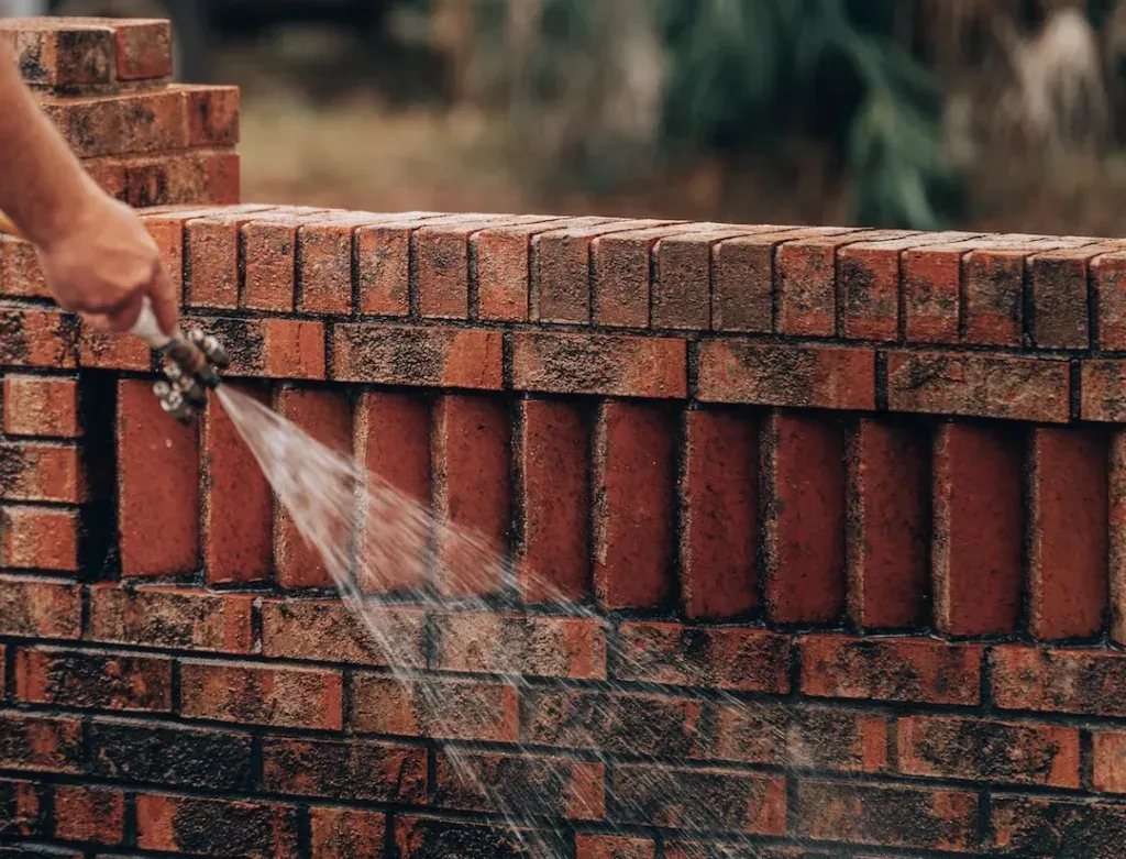 A person is spraying water on a brick wall with a hose.