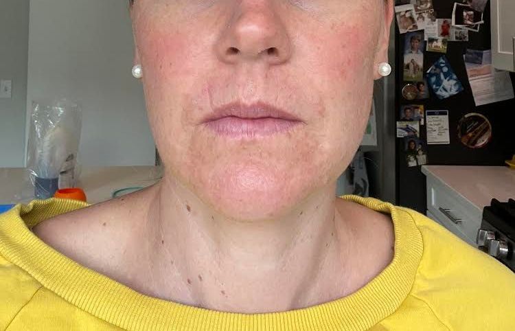 A woman in a yellow sweater is taking a selfie in a kitchen.