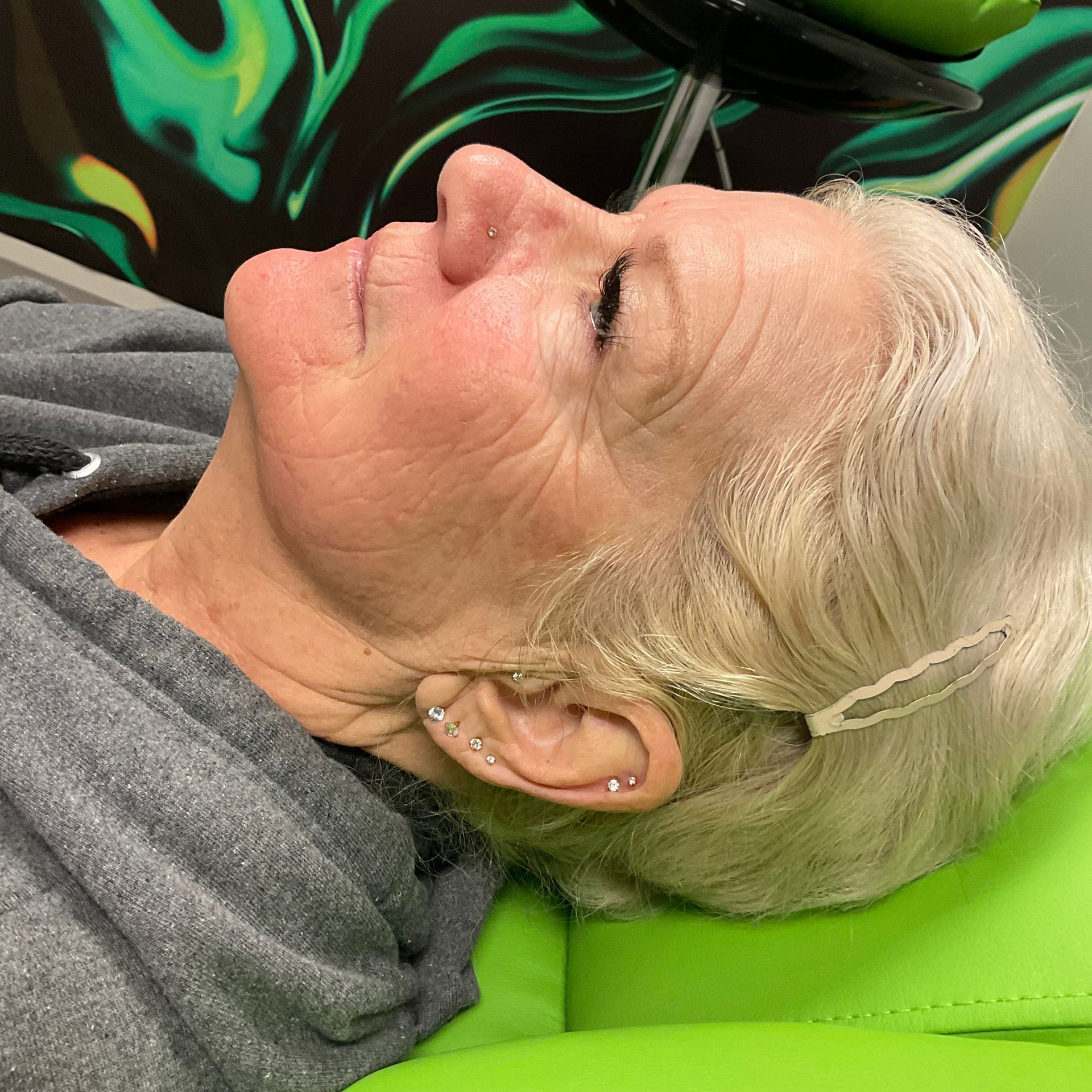 An older woman is laying on a green chair with her eyes closed.
