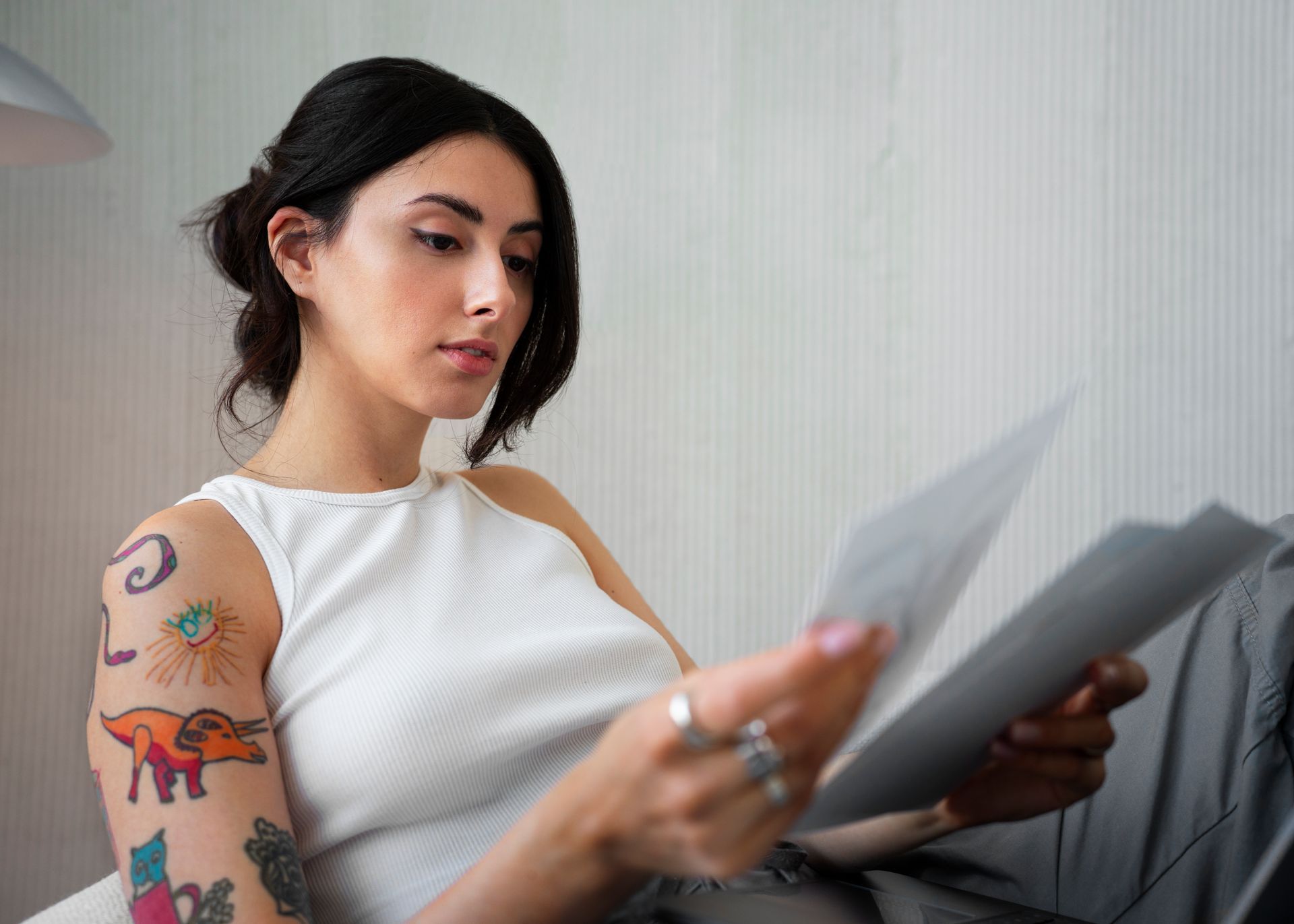 a woman with tattoos on her arms is sitting on a couch reading a piece of paper .