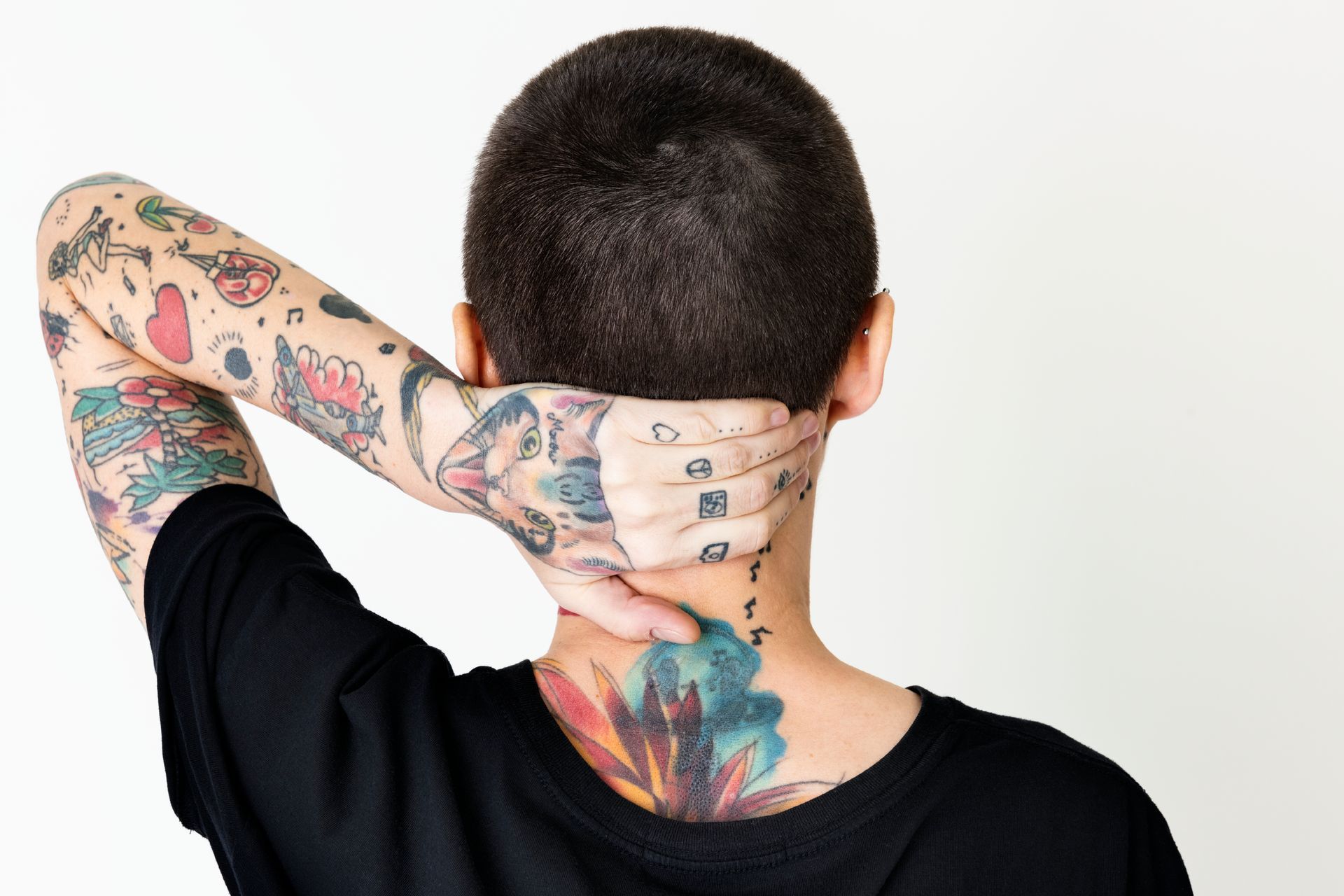 Person with tattoos on arm and neck, hand behind head, wearing a black shirt.