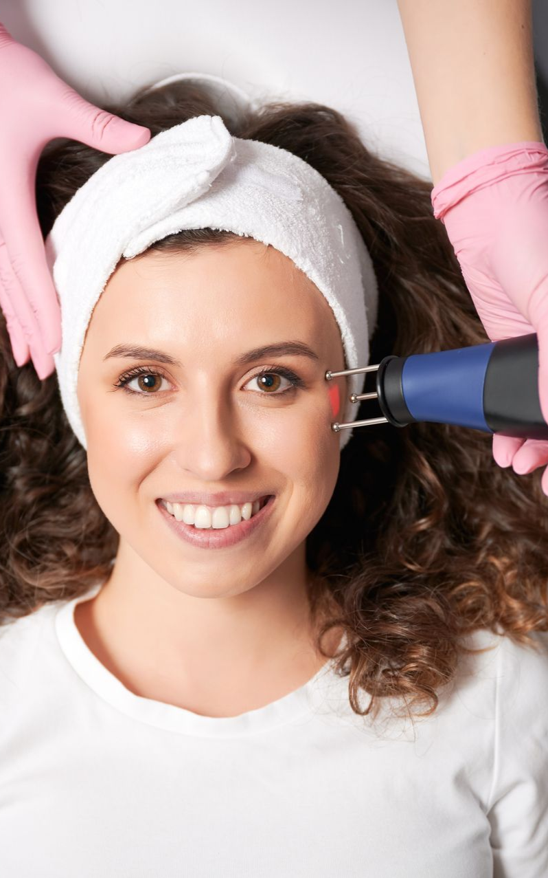 Woman undergoing facial skin treatment with a handheld device, smiling.