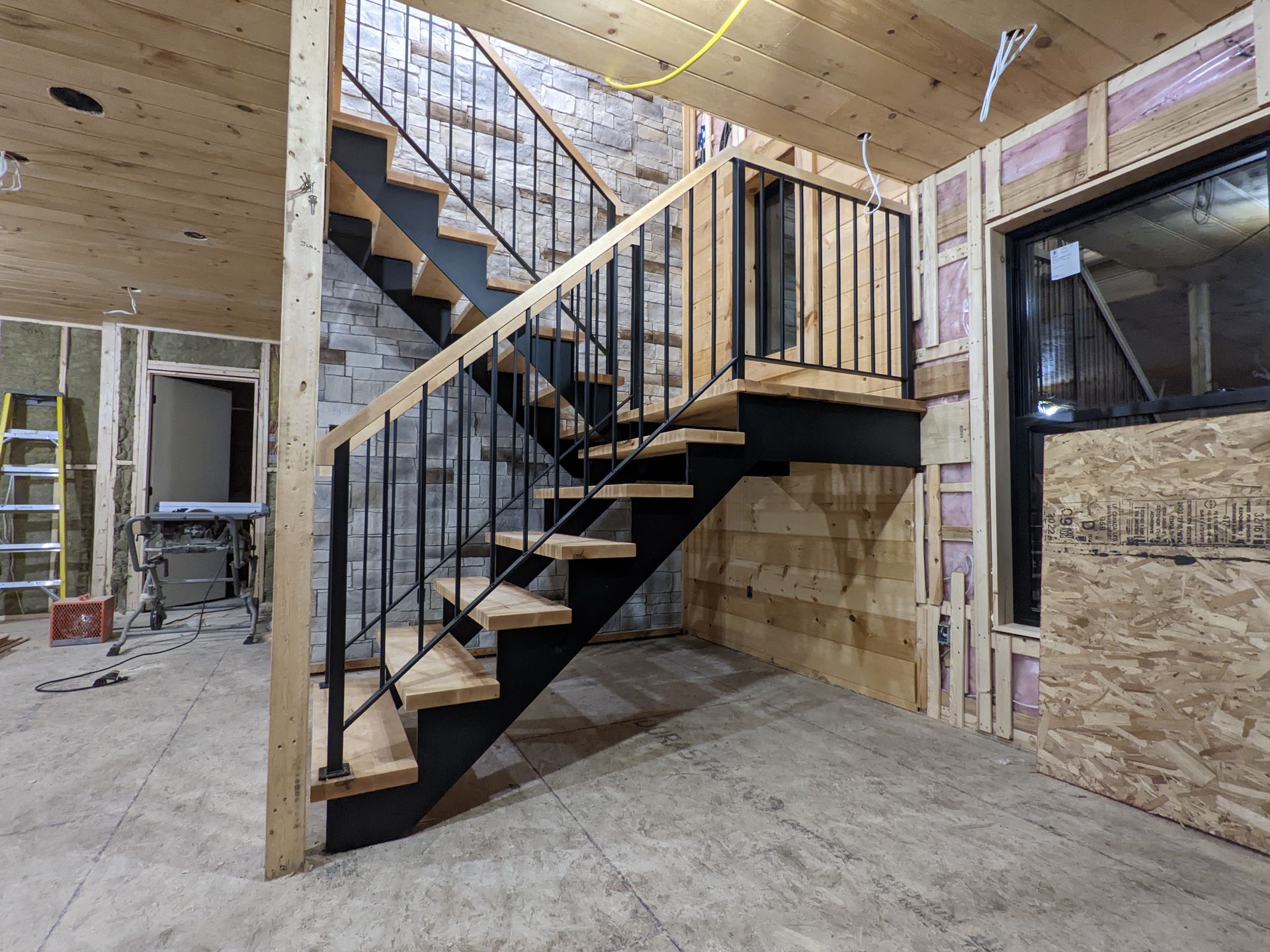 Un escalier en bois avec une rampe métallique dans une pièce en construction.