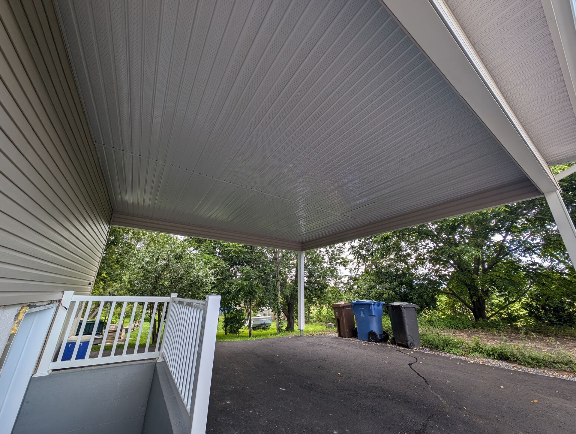 Un abri pour voiture avec une balustrade blanche et des poubelles en dessous.