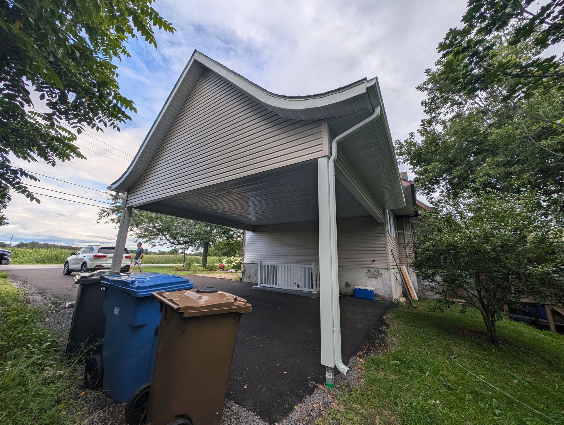 Une poubelle se trouve sous un auvent devant une maison.