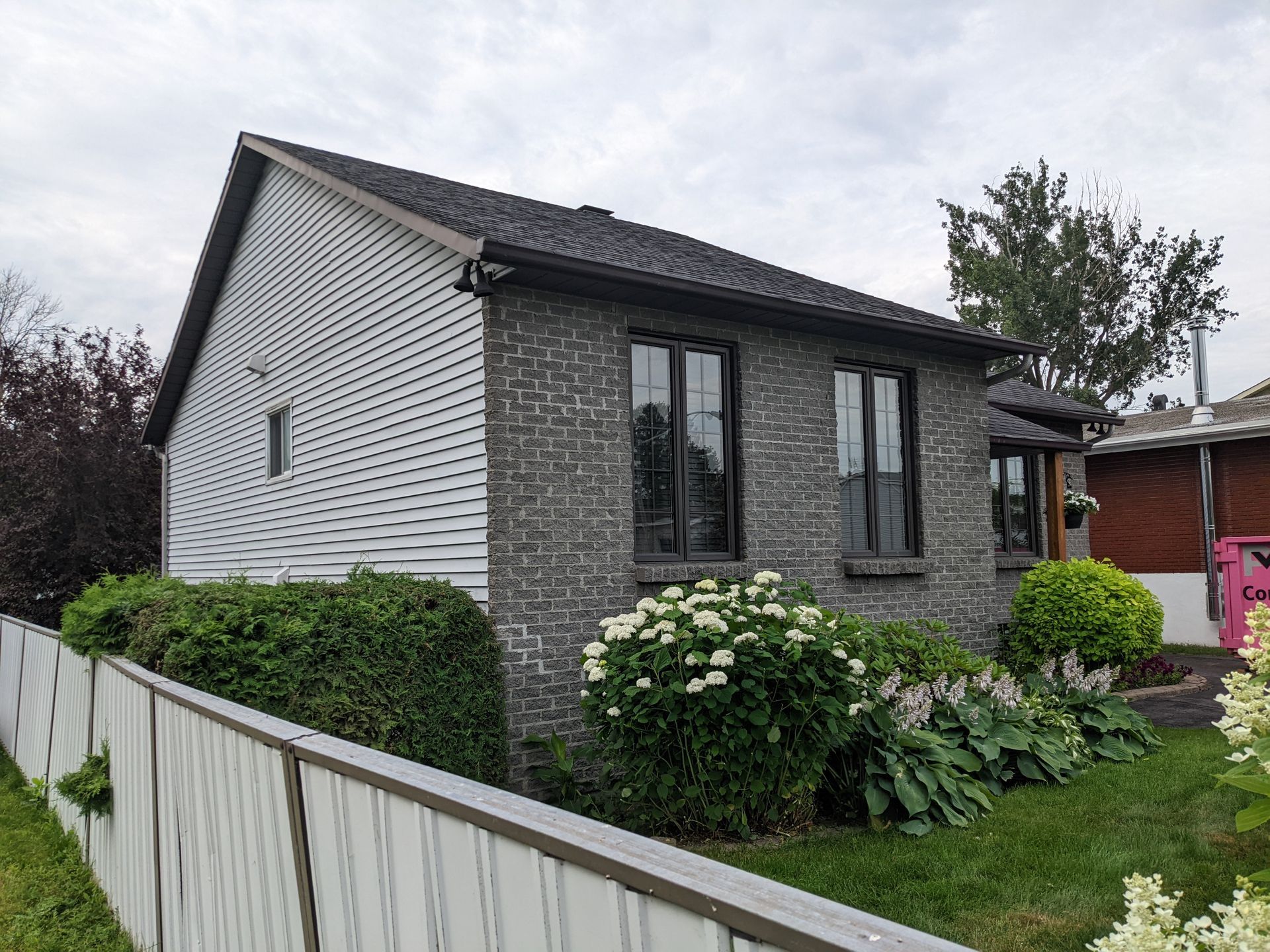 Une petite maison en brique avec une clôture blanche devant.