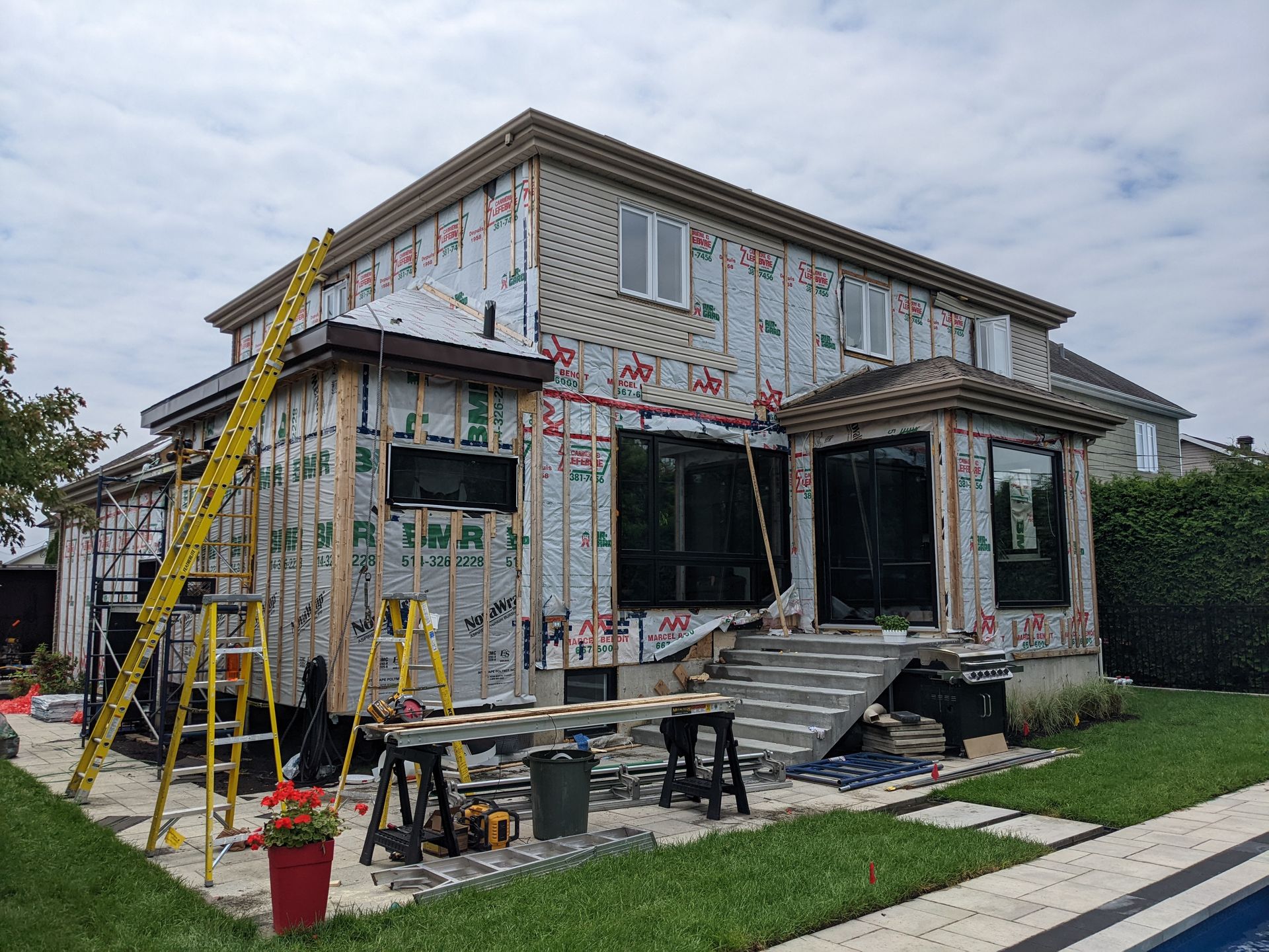 Une grande maison est en cours de rénovation dans une cour à côté d'une piscine.