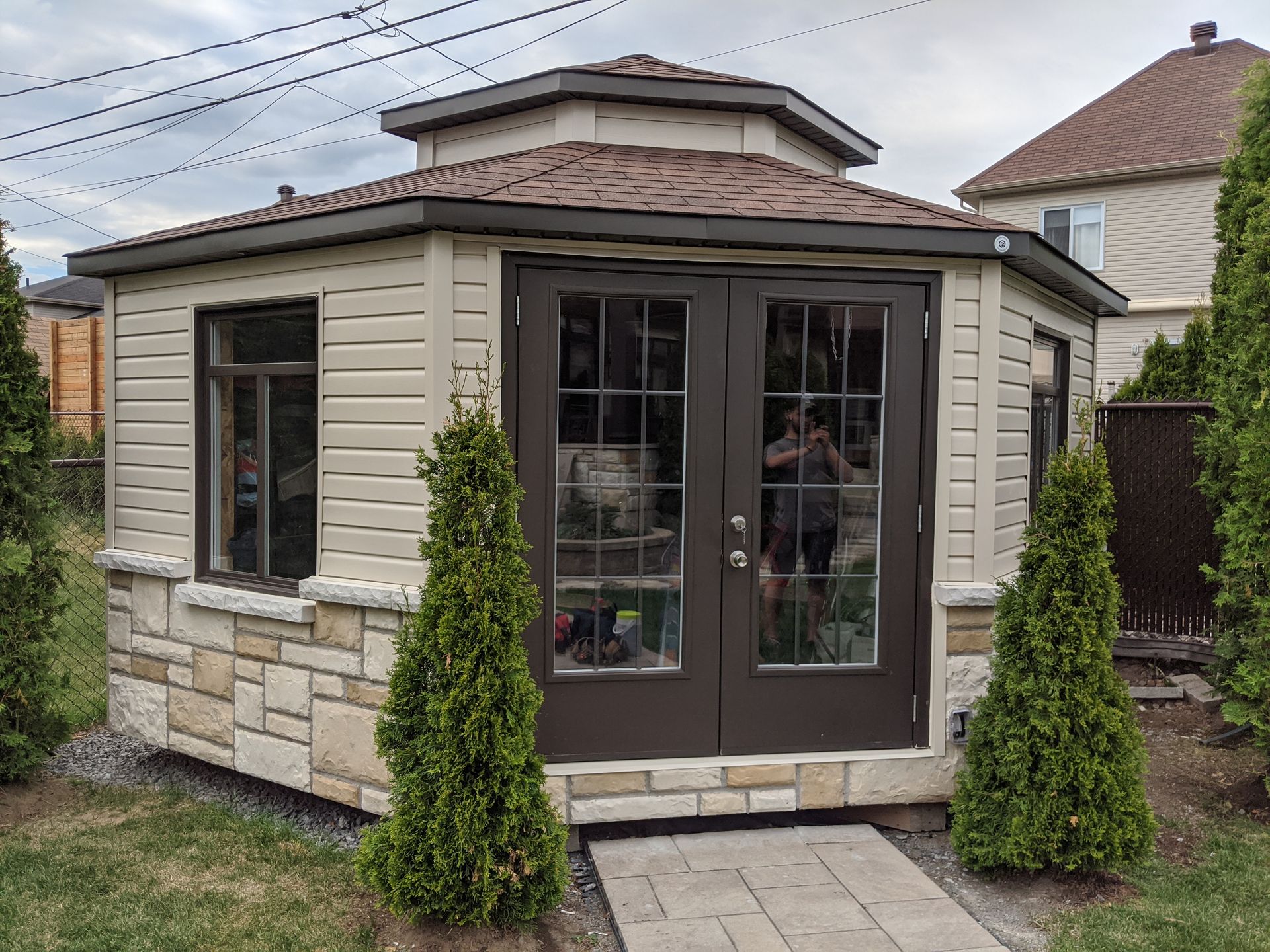 Une petite maison au toit marron est entourée d'arbres dans une cour.