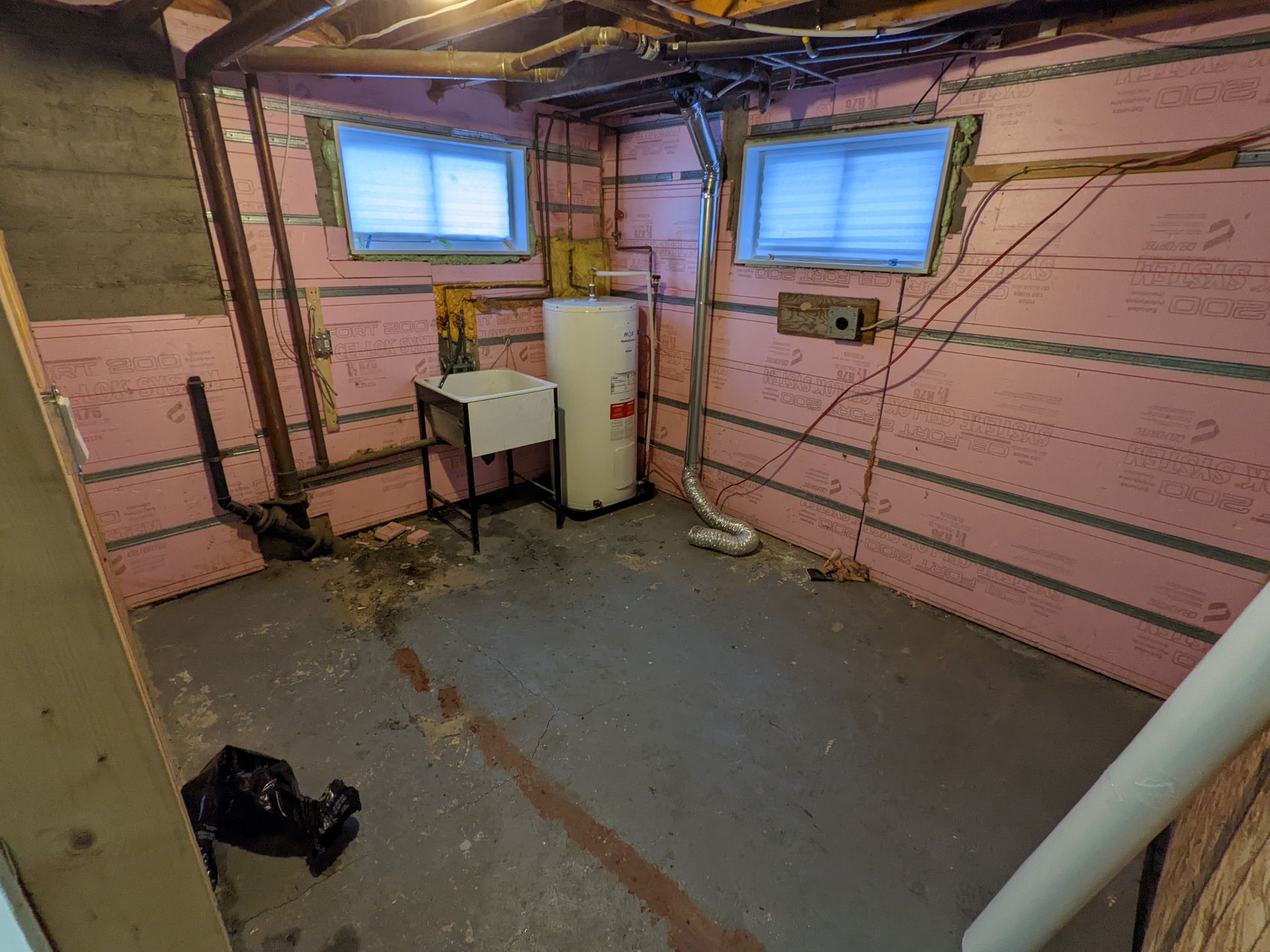 Un sous sol avec isolation rose et un chauffe eau.