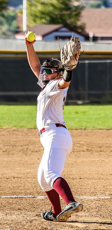 A person wearing a hat and orange shirt, holding a baseball bat on their shoulder on a baseball field.