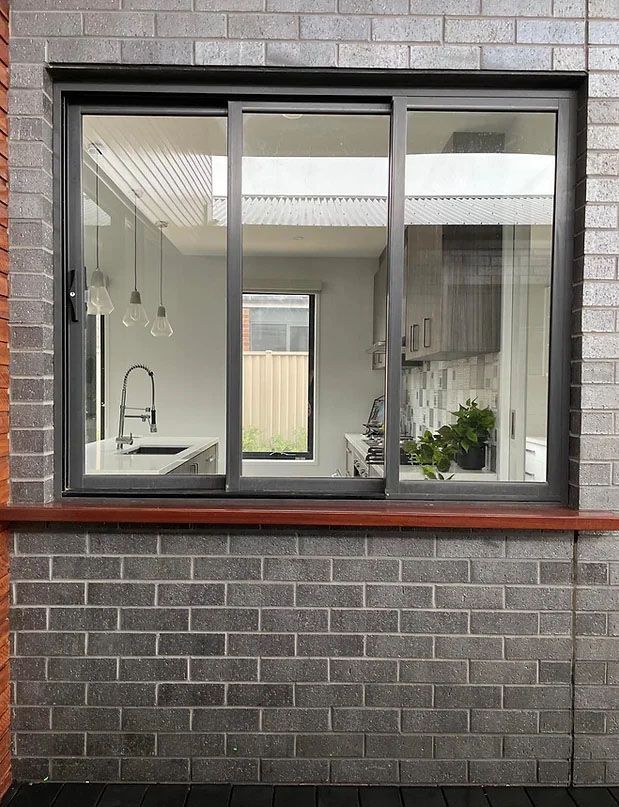 A Brick Wall With a Sliding Glass Window Looking Into a Kitchen — Evoke Building Group In Ballarat Central, VIC