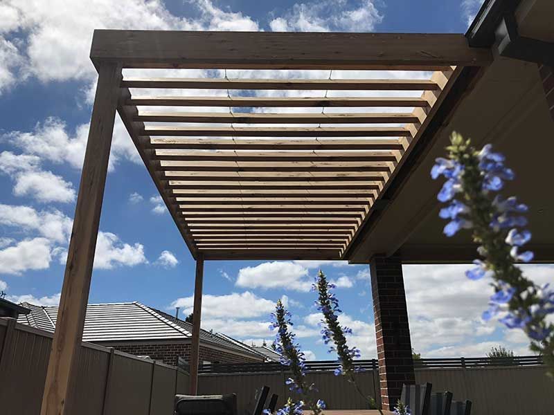 A Wooden Pergola is Sitting on Top of a Patio With a Table and Chairs Underneath It — Evoke Building Group In Ballarat Central, VIC