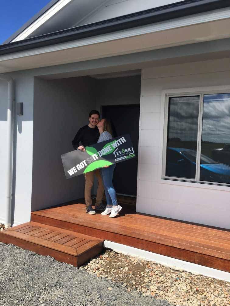 A Man and a Woman Are Standing in Front of a House Holding a Sign — Evoke Building Group In Ballarat Central, VIC