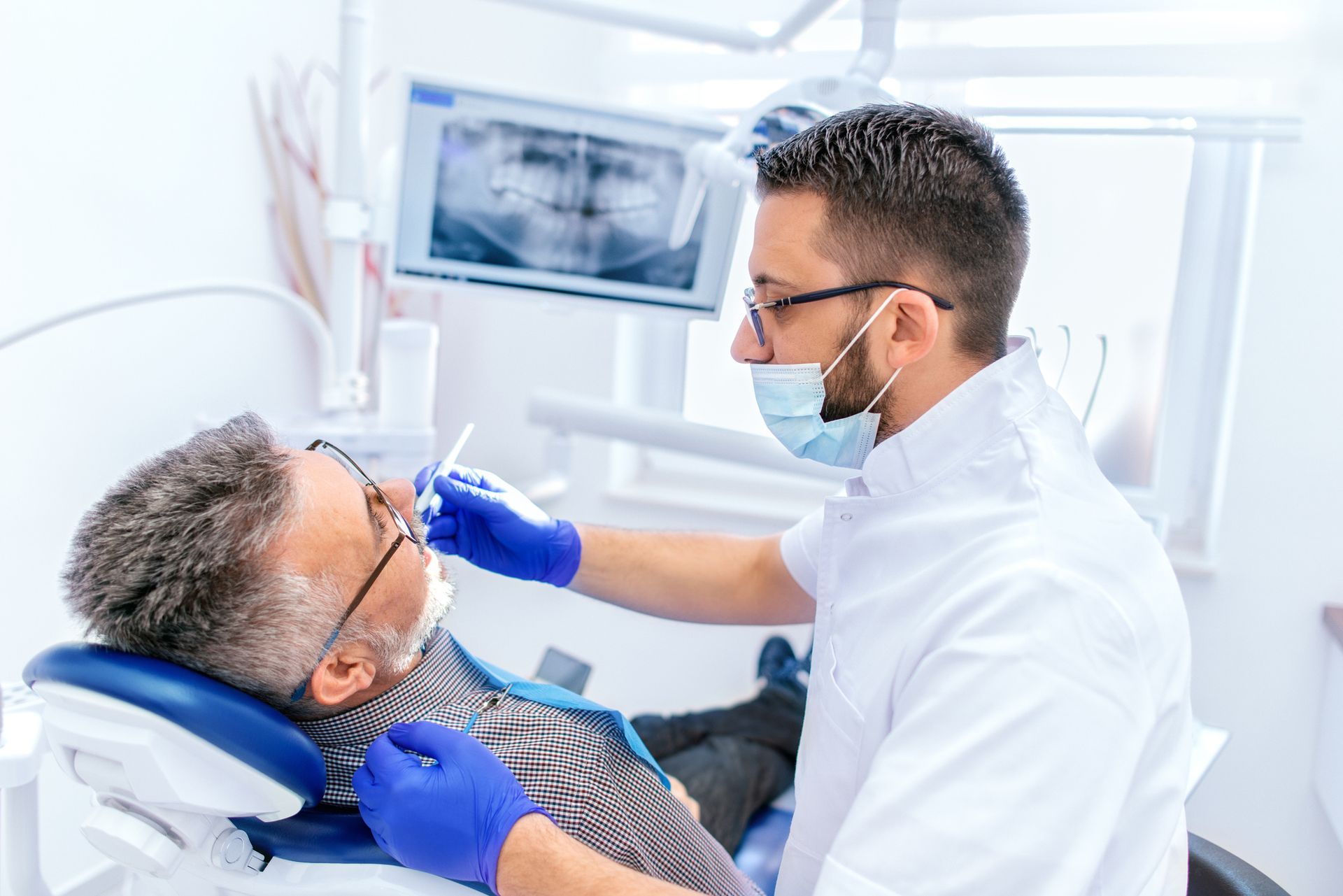 A man sits in a dental chair while a periodontist inspects his teeth for health issues. A man sits in a dental chair while a periodontist inspects his teeth for health issues.