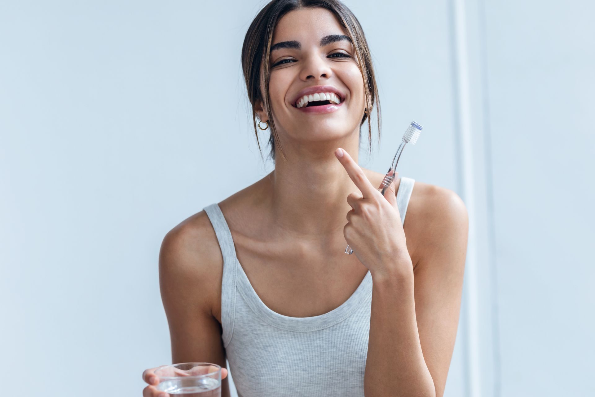 A woman is holding a glass of water and a toothbrush.