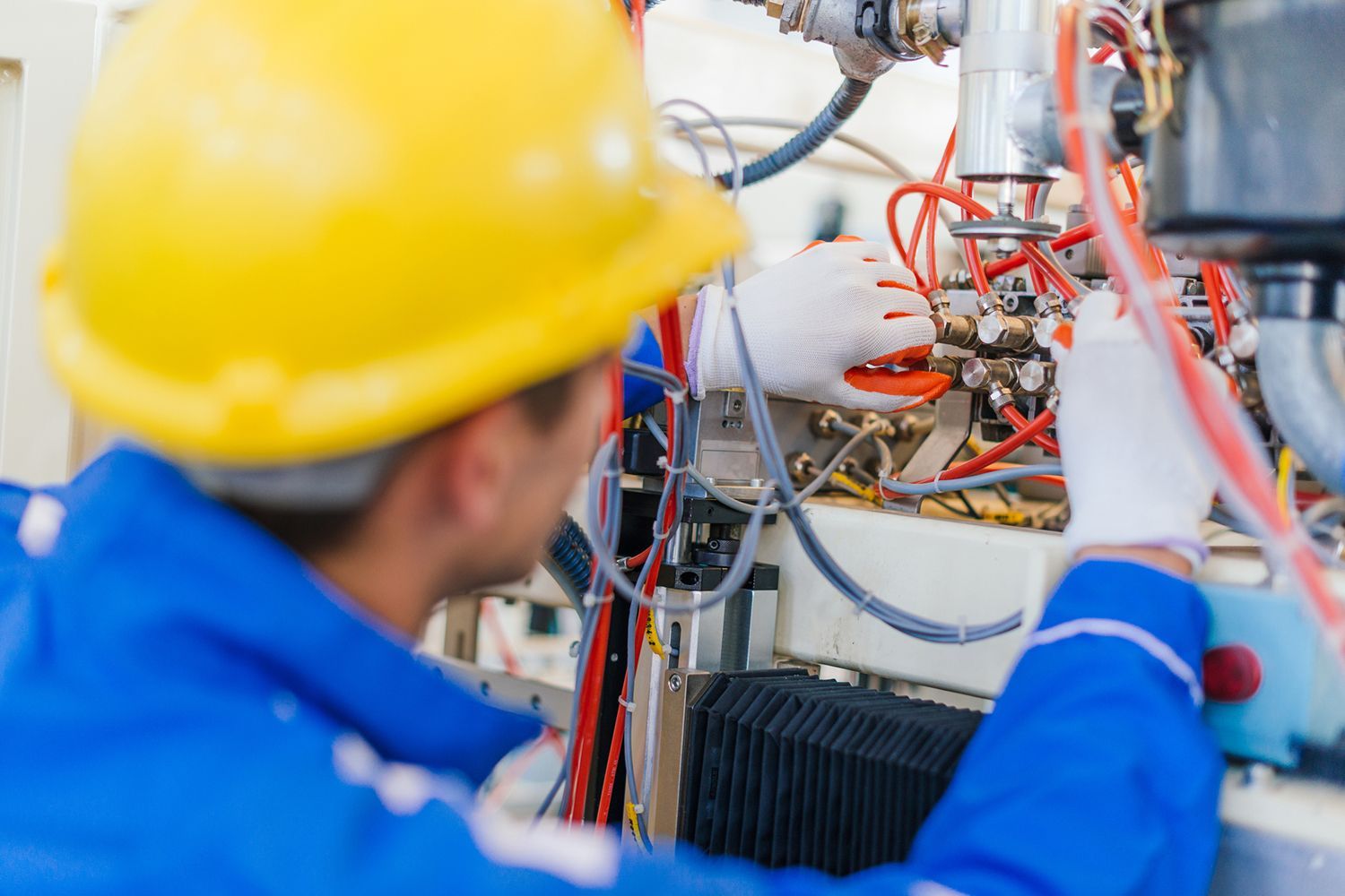 A man wearing a hard hat is working on a machine in a factory.