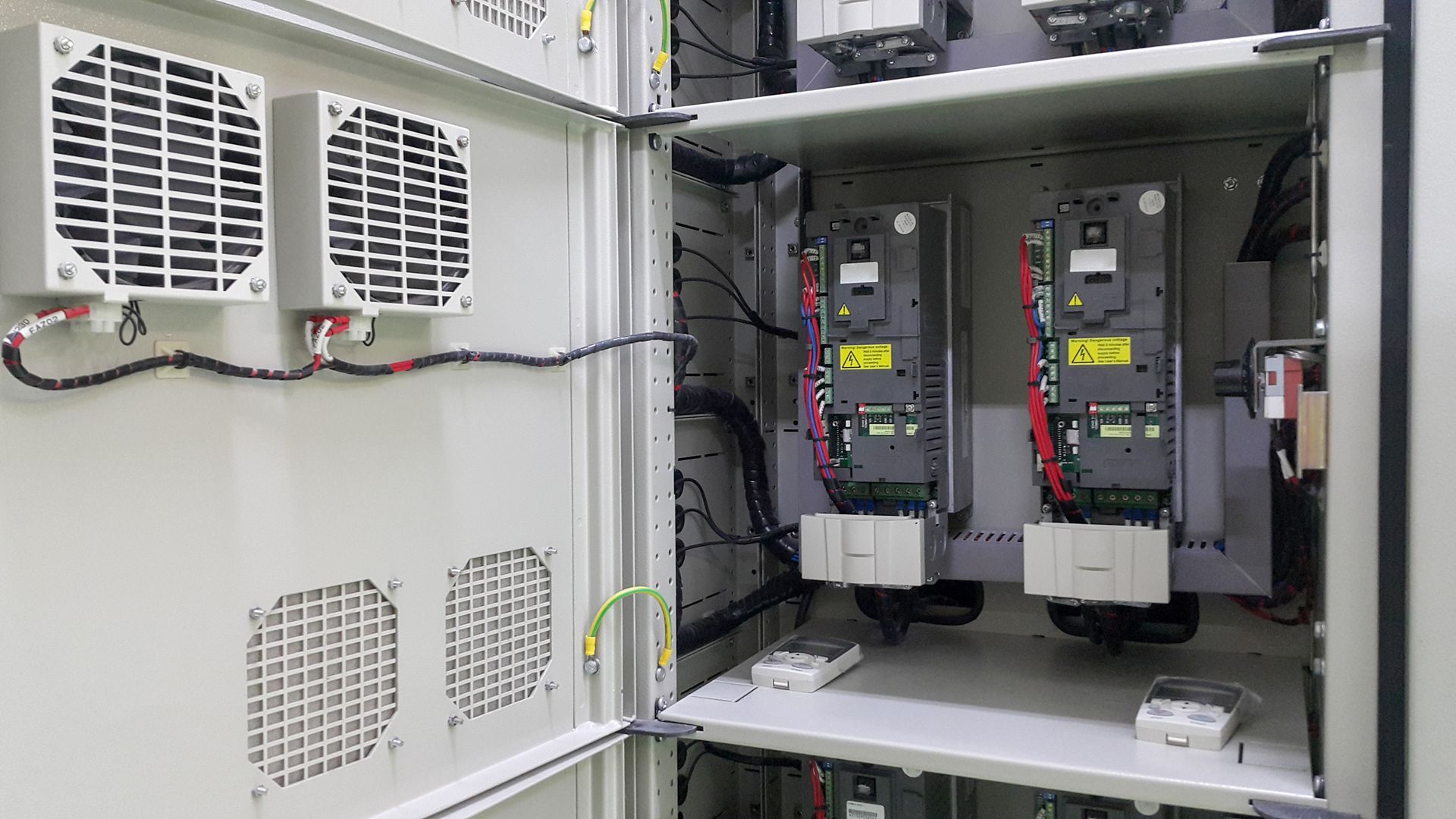Open electrical panel showing dual VFD units with connected power cables and cooling fans.