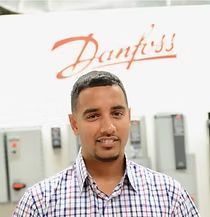 A man in a plaid shirt is standing in front of a danfoss sign.