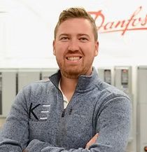 A man is standing with his arms crossed in front of a danfoss sign.